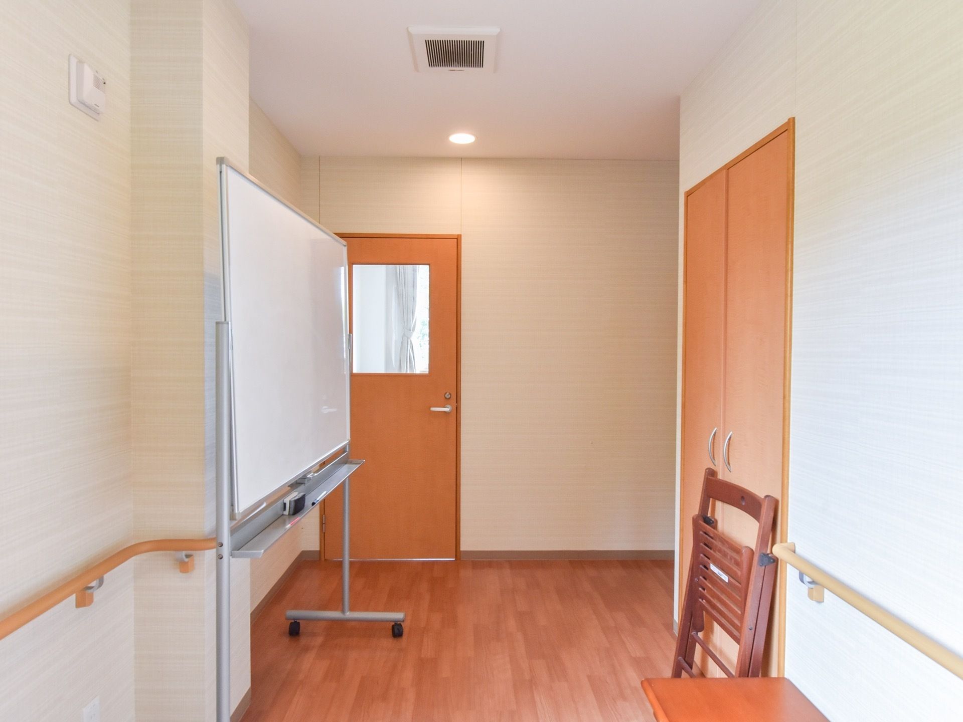 通路には白い壁に手すりがつき、天井換気扇や火災報知器もある。移動式の白板とベンチなどが置かれている。