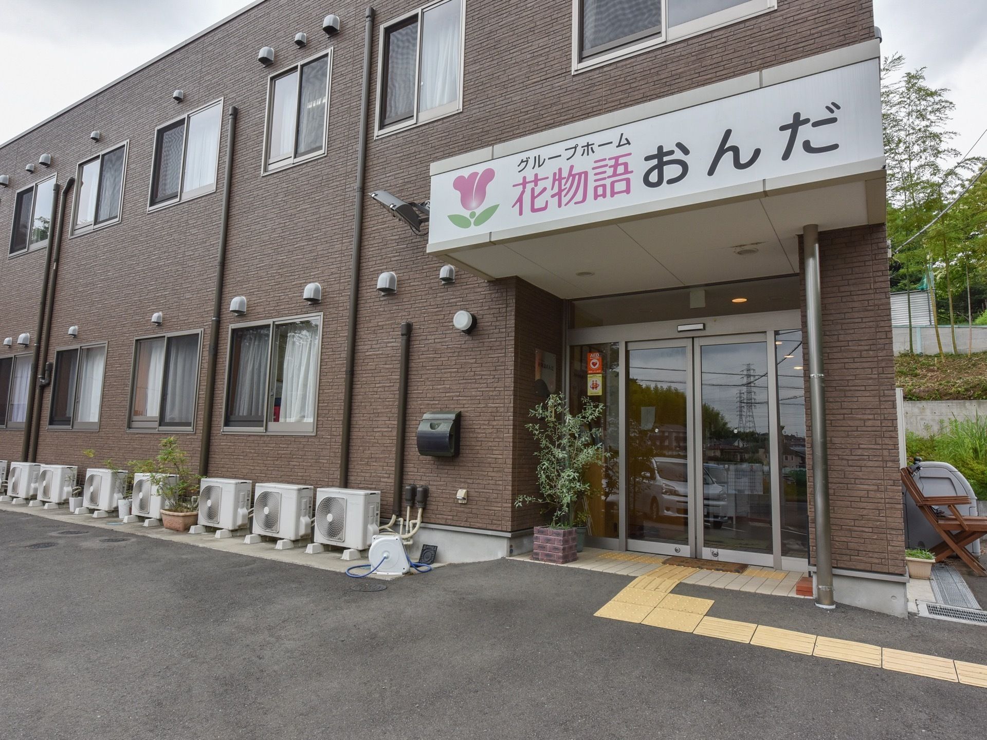 ダークブラウンの２階建ての建物である。横側に玄関を設け、上部の側面に大きな文字で施設名を表示している。