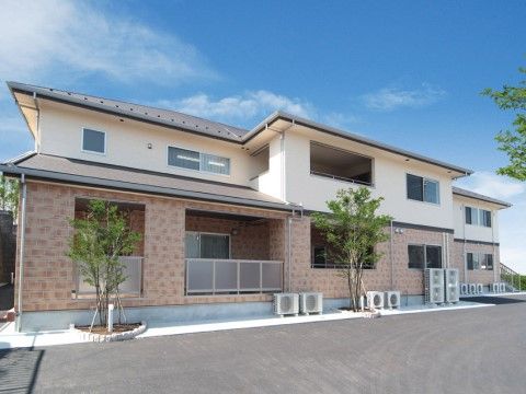 裏にコンクリート張りの広い駐車スペースがある2階建ての施設
