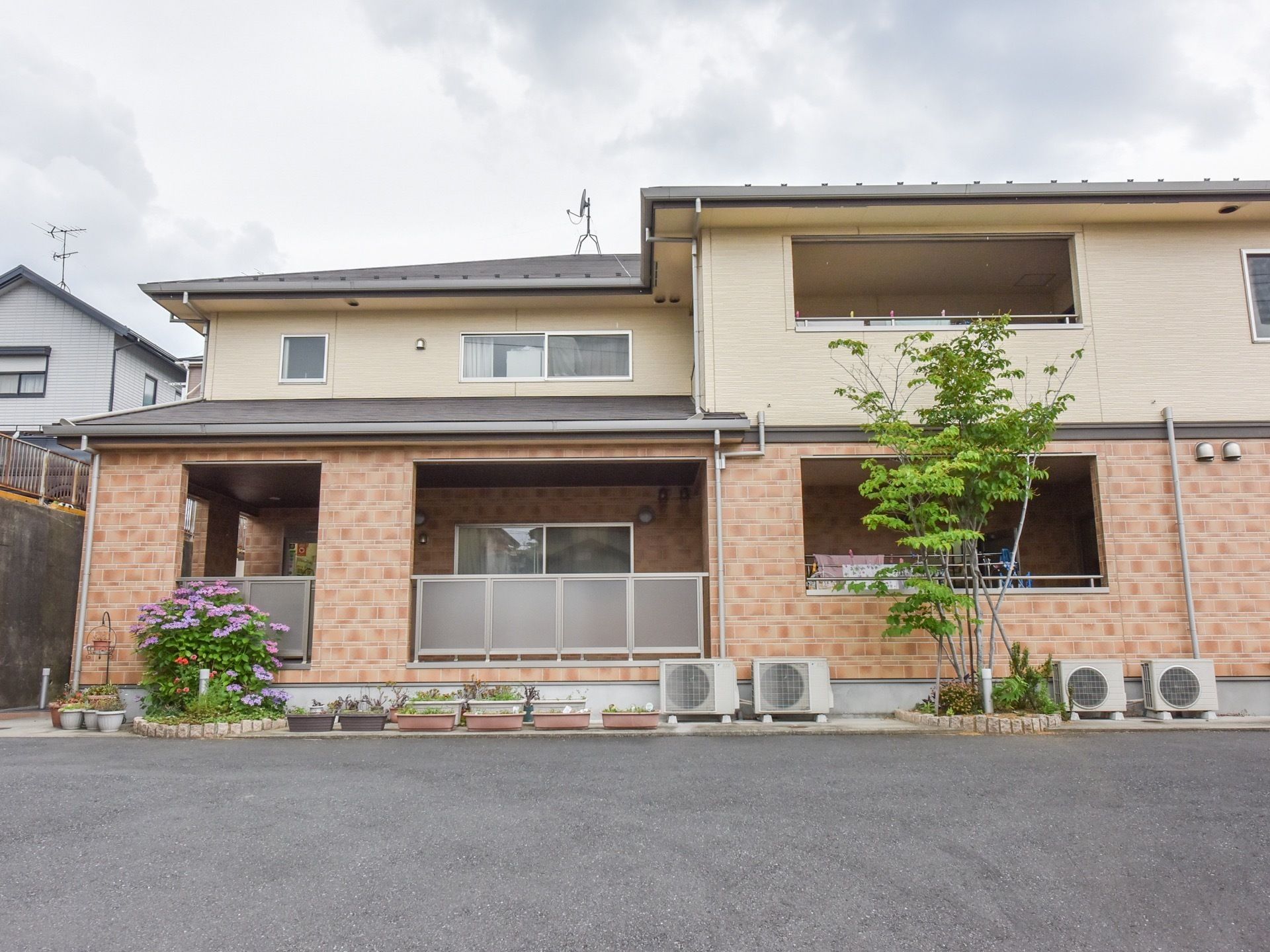 白とピンクの外壁が特徴の２階建ての建物である。周辺には鮮やかな草花が植えられており、華やかな外観である。
