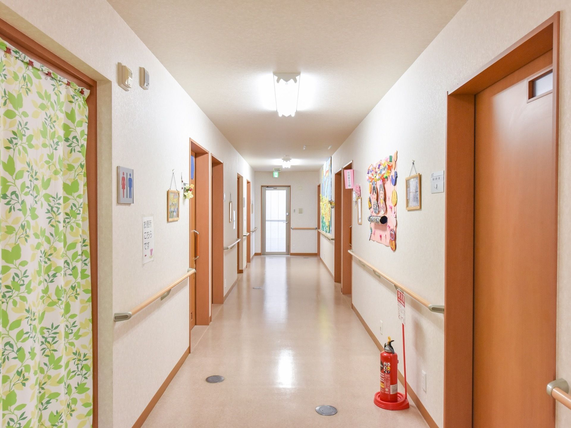 廊下には手すりが完備されており、歩行する入居者様の手助けをしている。道幅は広く、車椅子が２台通れるほどである。