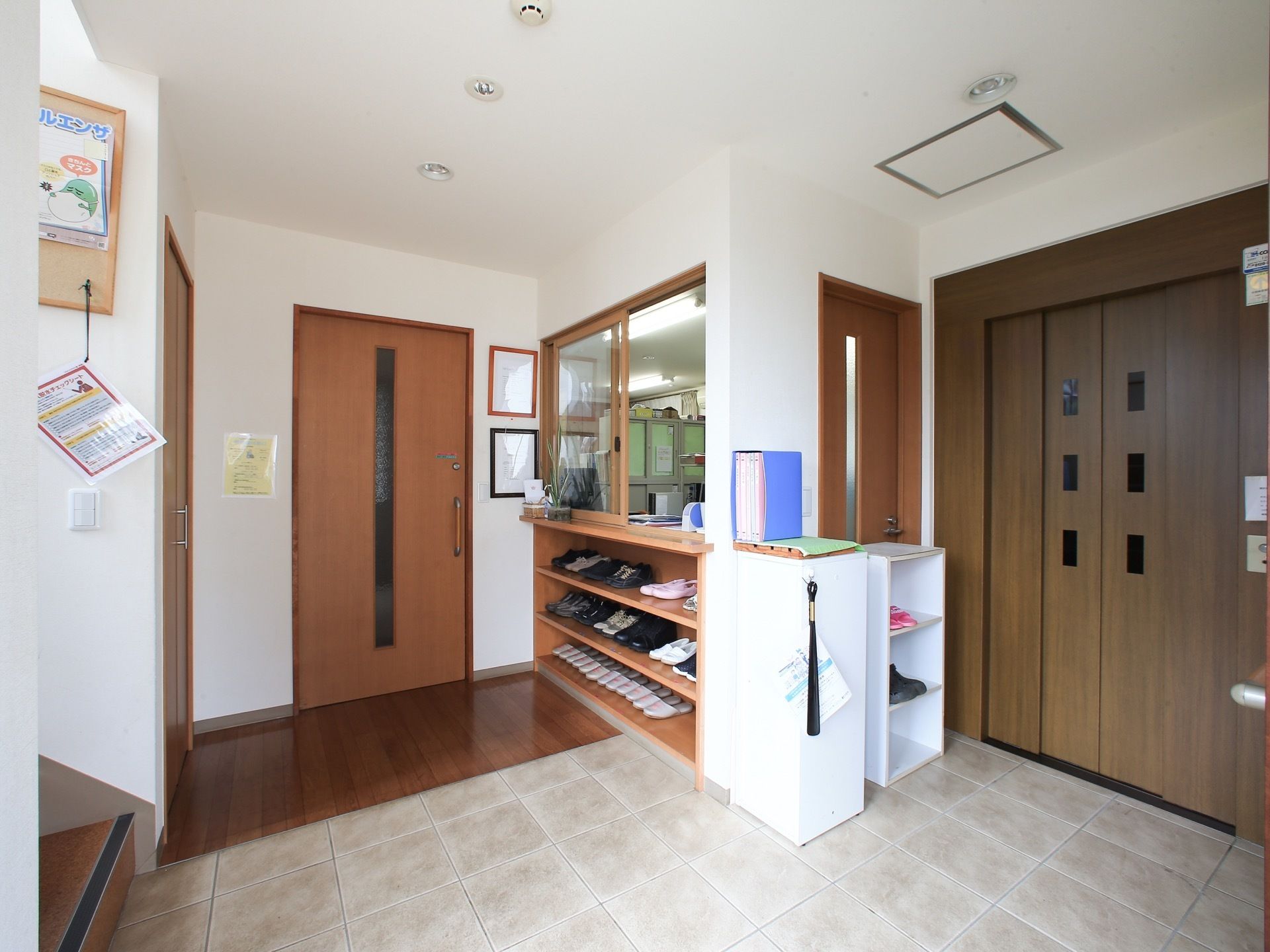 施設内部とはスライド式の扉で仕切られている。受付窓口の下部に３段の棚を設けてあり、下駄箱として利用されている。