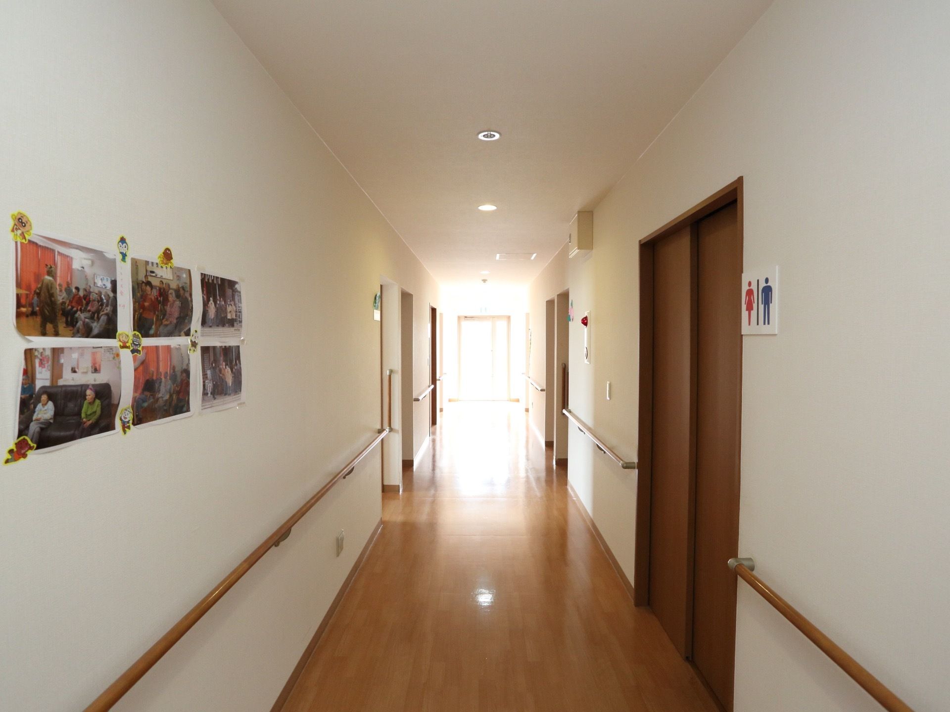 通路の右側には茶色い扉のトイレがあり、横には男性と女性のシルエットが書かれたプレートが貼られている。壁の左側には６枚の写真がある。