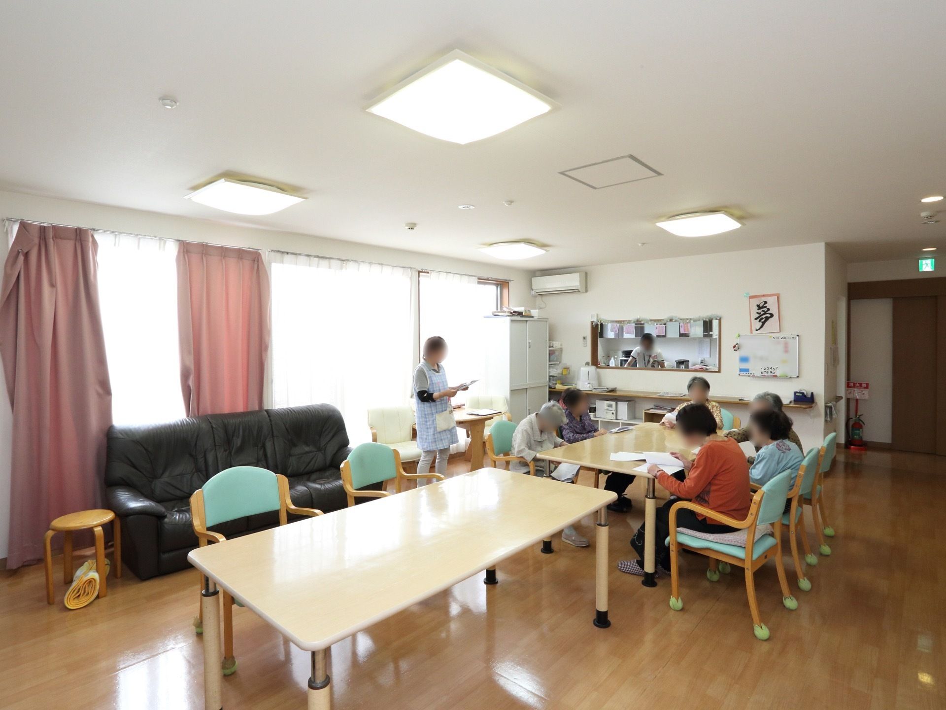 食堂にはテーブル２台が置かれている。ミントグリーンの背もたれが付いた椅子には６人の入居者様が座っている。