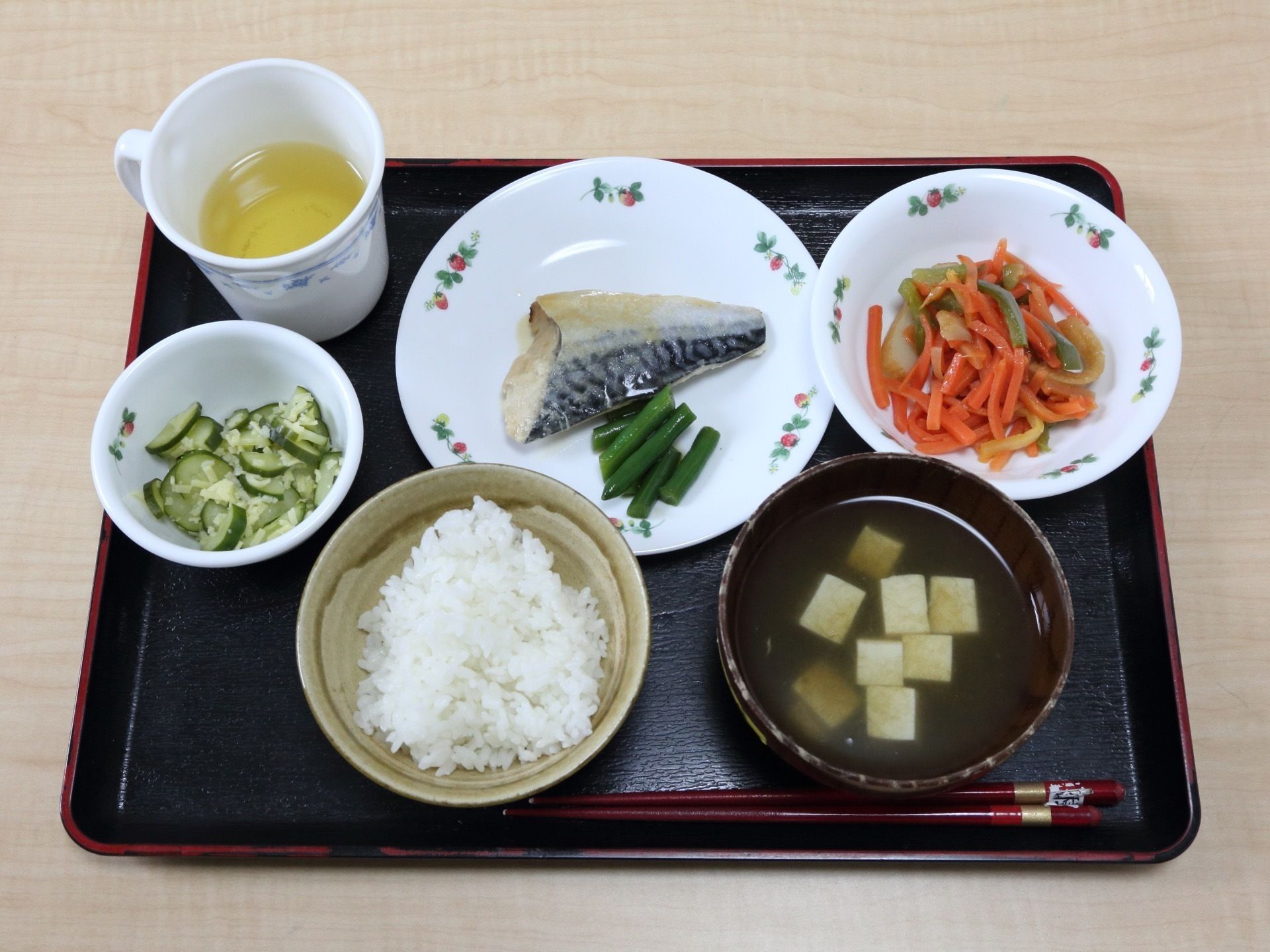 黒いお盆の上にはお茶、お箸、ご飯、お味噌汁、おかずが並べられている。メインは魚で、野菜２品のおかずである。