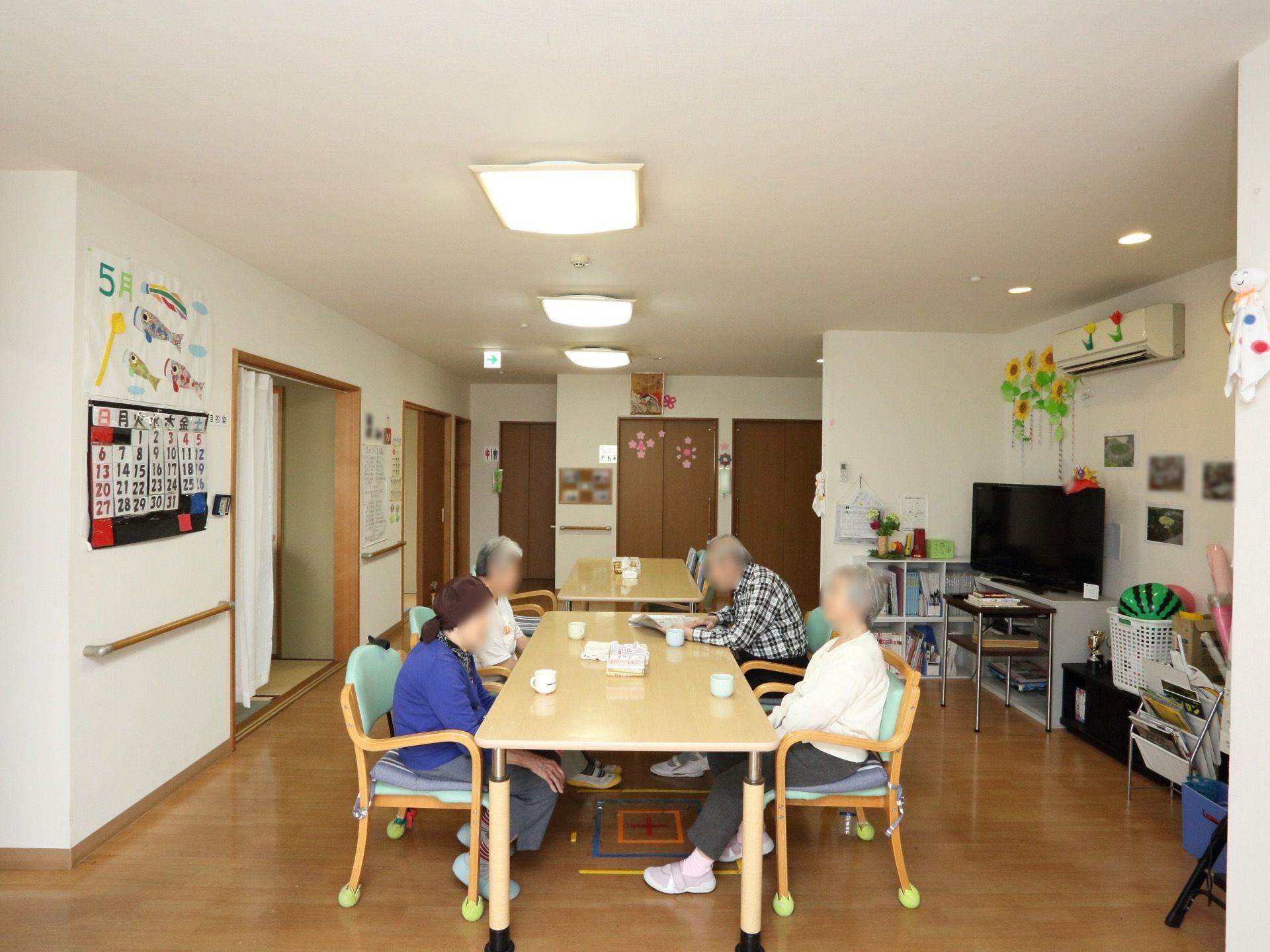 食堂にはテーブル、椅子が並べられている。壁には５月の文字と鯉のぼりのイラストがある。下には手作りのカレンダーが貼られている。