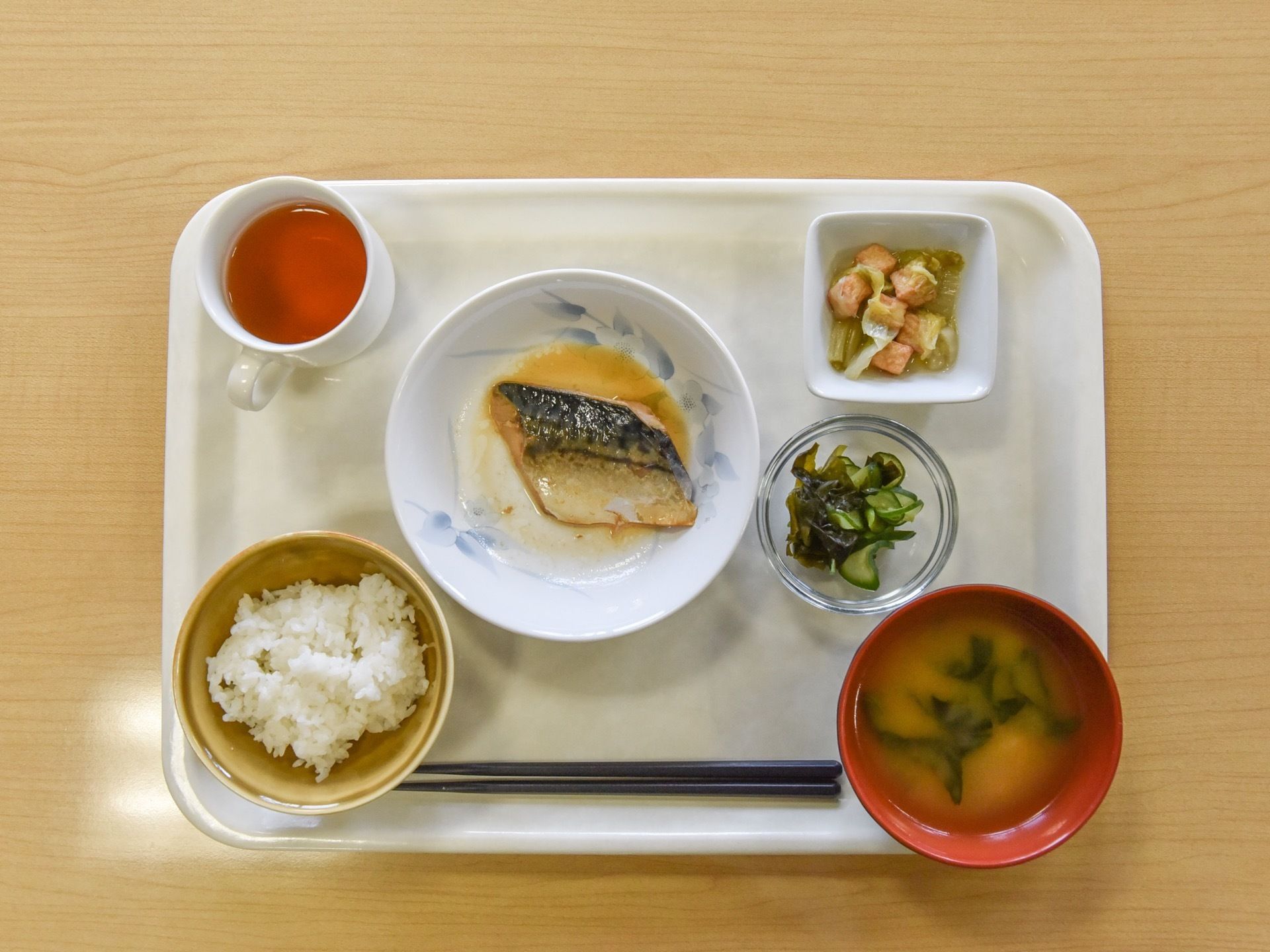 白く四角いトレイに小鉢に盛り付けられた料理が乗せられている。煮魚やみそ汁や白米など和食中心の献立である。