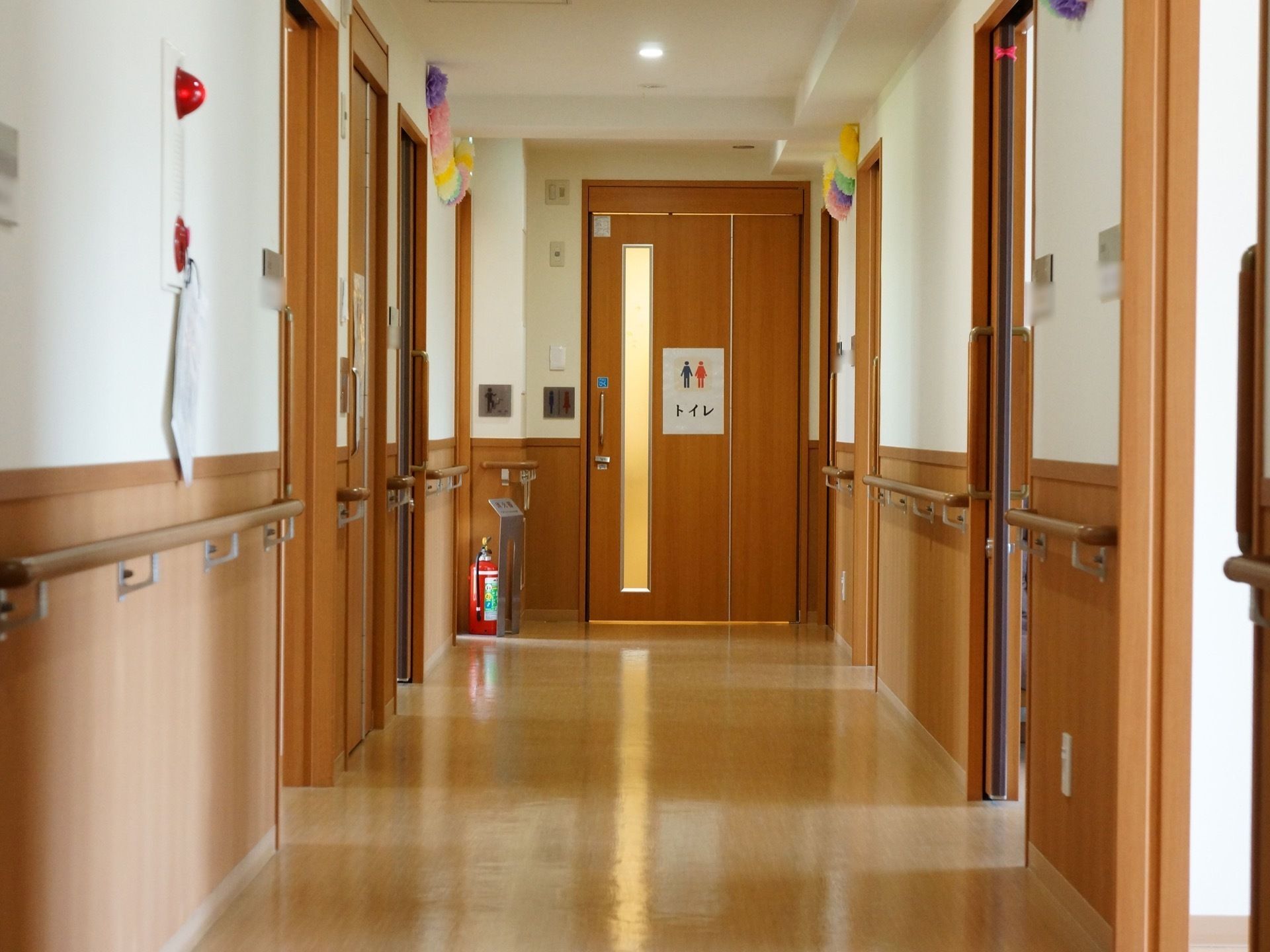 幅が広めの通路。両側の壁には手すりが設置されている。通路正面の引き戸には大きく「トイレ」と書かれた案内が貼られている。