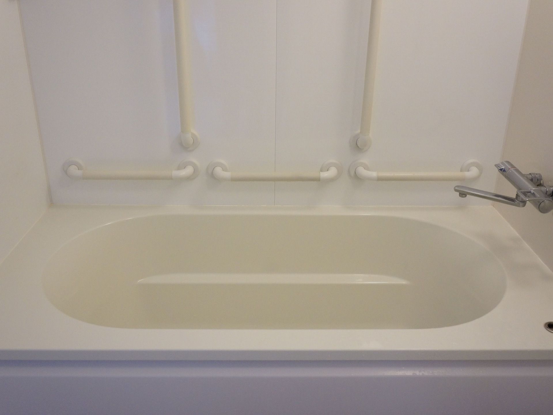 低くて広めの浴槽に縦向きの手すりが２本、横向きの手すりが３本設置してある。浴槽にお湯をためるための蛇口がついている。