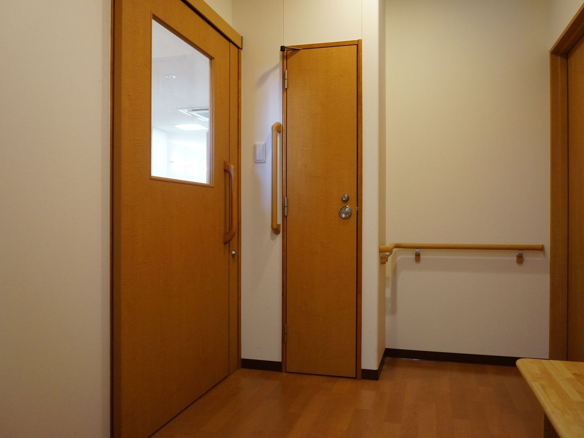 白い壁にフローリングの床の通路。各入口のドアは木製である。壁の必要な部分には手すりが取り付けられている。