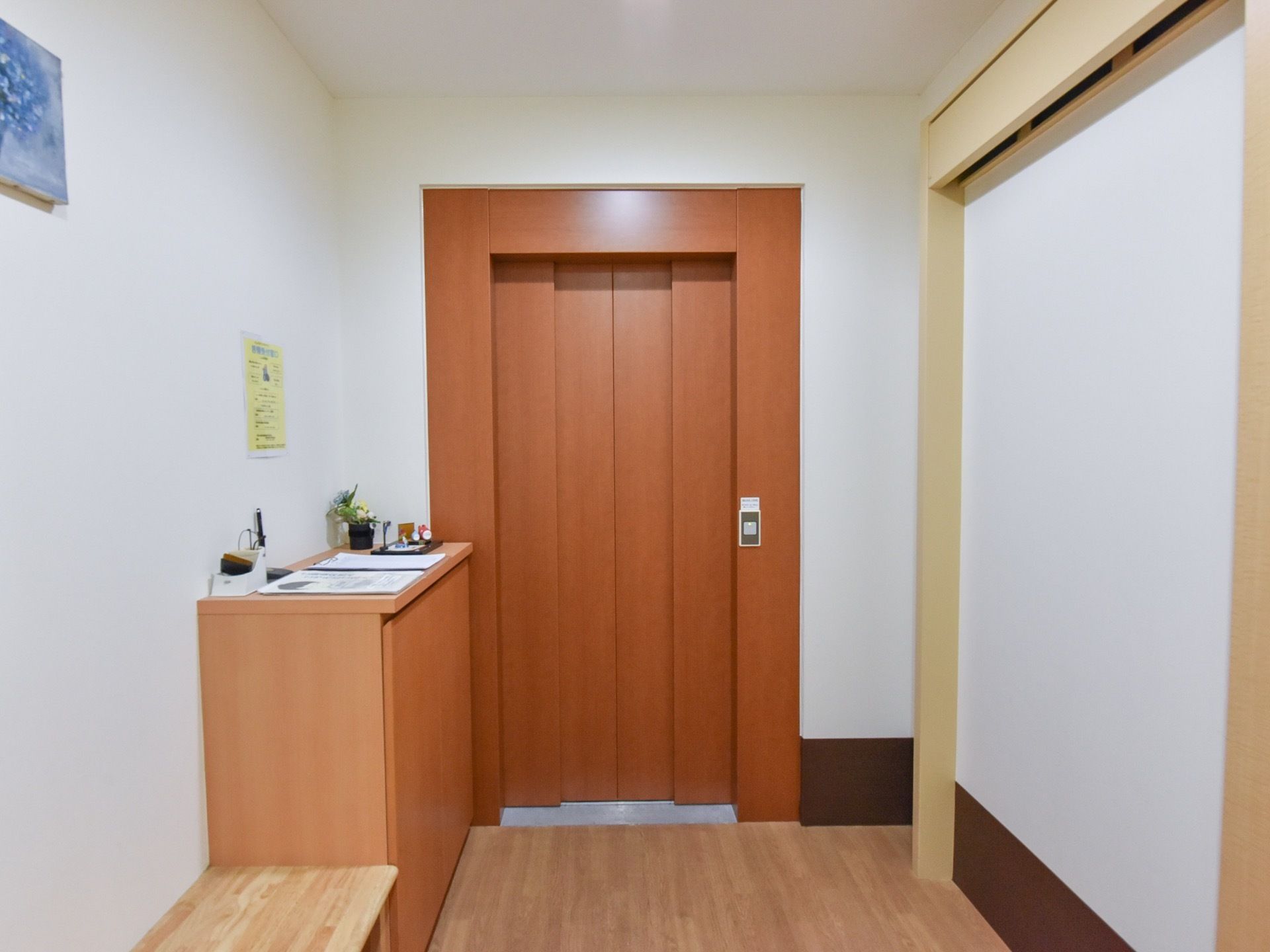 床はバリアフリー構造となっている。扉のすぐ横にはボタンが設置されている。扉前には棚がありその上には花や小物が飾られている。