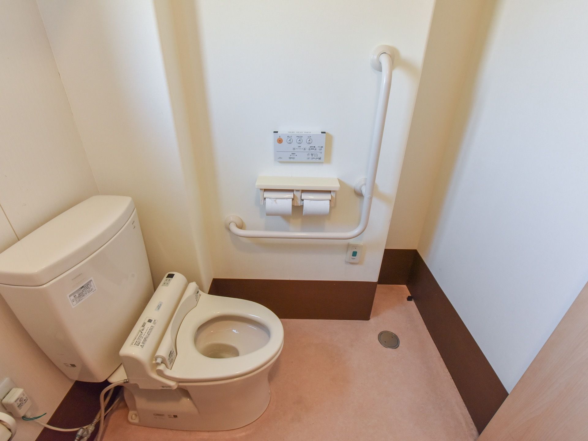 トイレットペーパーホルダーの上には温水洗浄便座のボタンが取り付けられている。その周囲にはL字の手すりが設置されている。