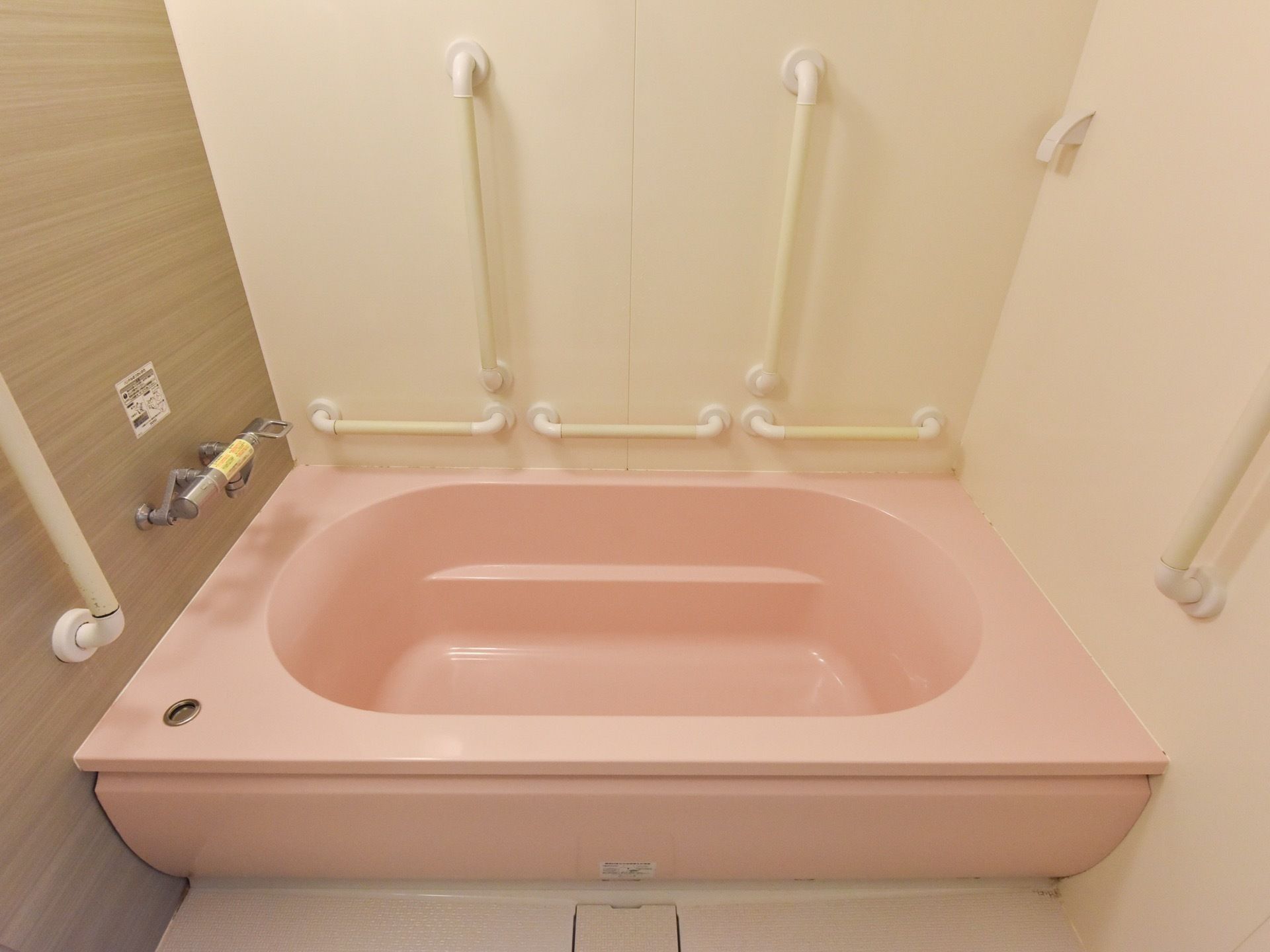 ピンク色の大きめの作りの浴槽である。浴槽内には腰掛ける場所がある。周囲はには手すりが設置されている。