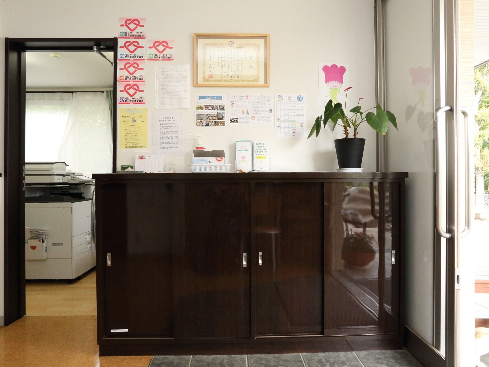 玄関の下駄箱の上に、入居者様の写真や行事のスケジュールを記した掲示物などが貼られている。床は段差がないので安心感がある。