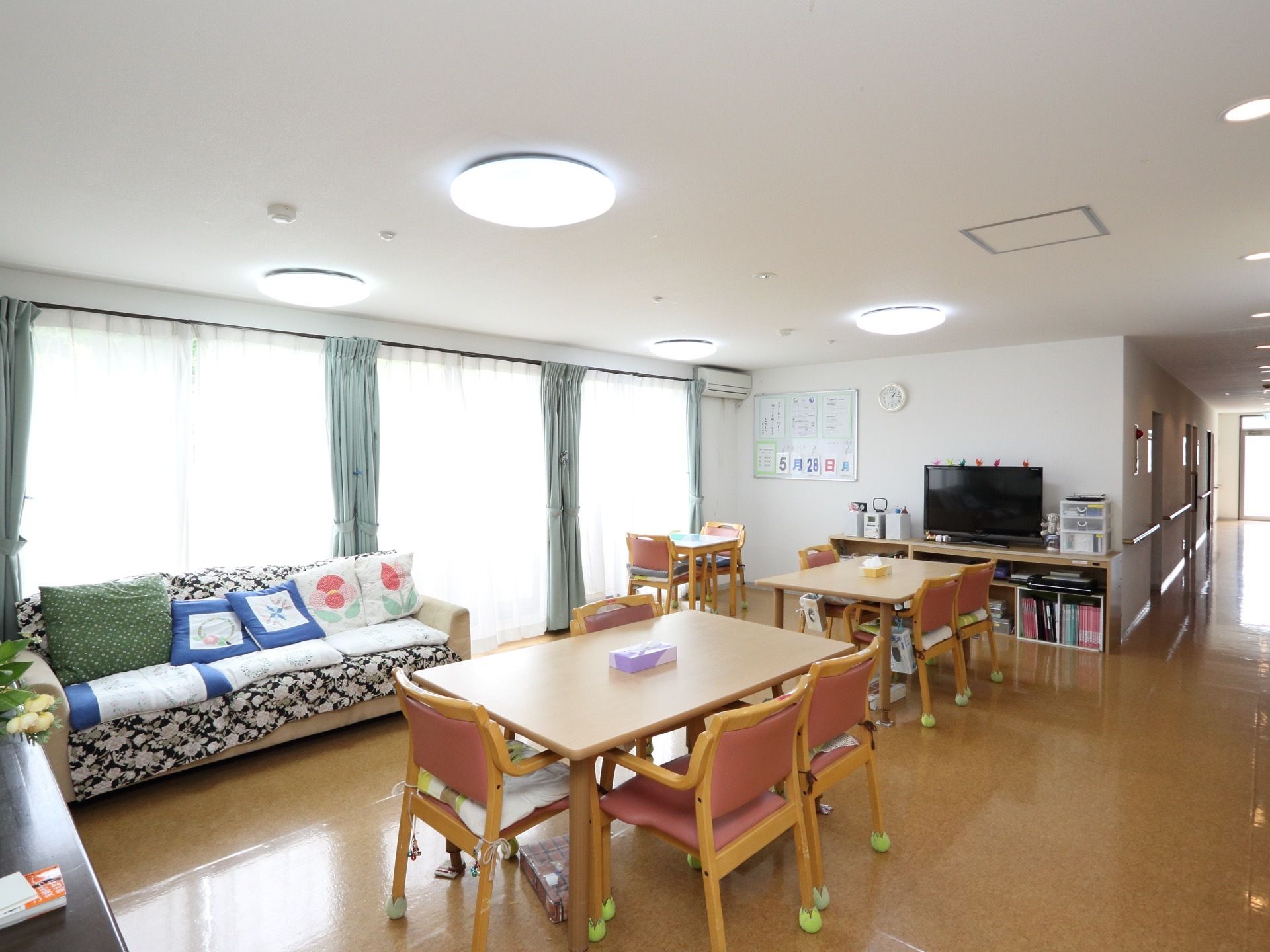 ソファーやテレビも設置されている共有スペースになっている。テーブルや椅子が並べられており、壁には掲示物が貼られている。