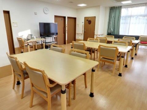 食堂には大きな窓があり、フローリングの床にはテーブルセットが置かれている。壁には手すりが設置され、大型テレビが置かれている。