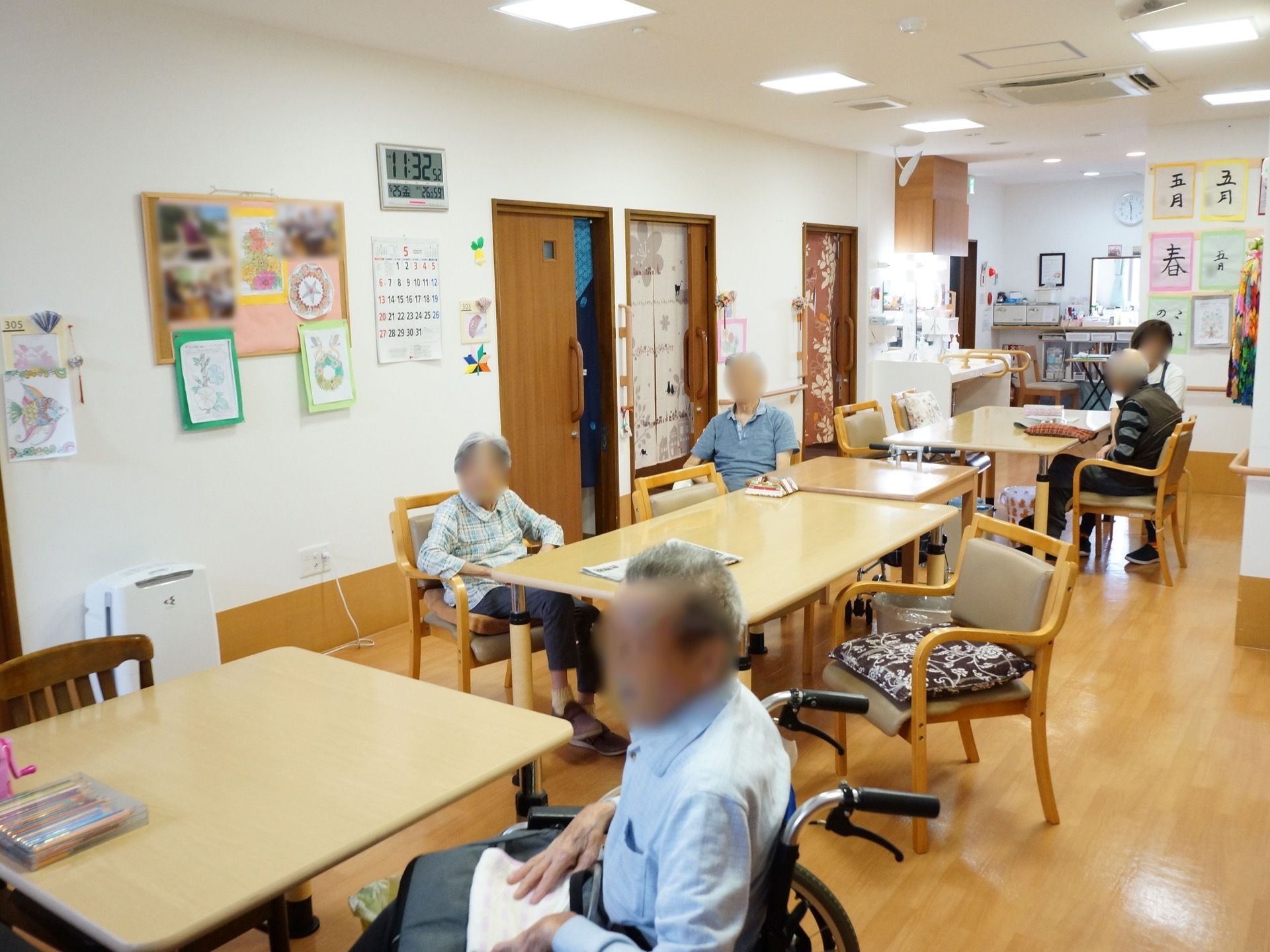 食堂兼共有スペースには、4つのテーブルと椅子が置かれ、奥には洗面台が設置されている。入居者様がくつろいでいる。