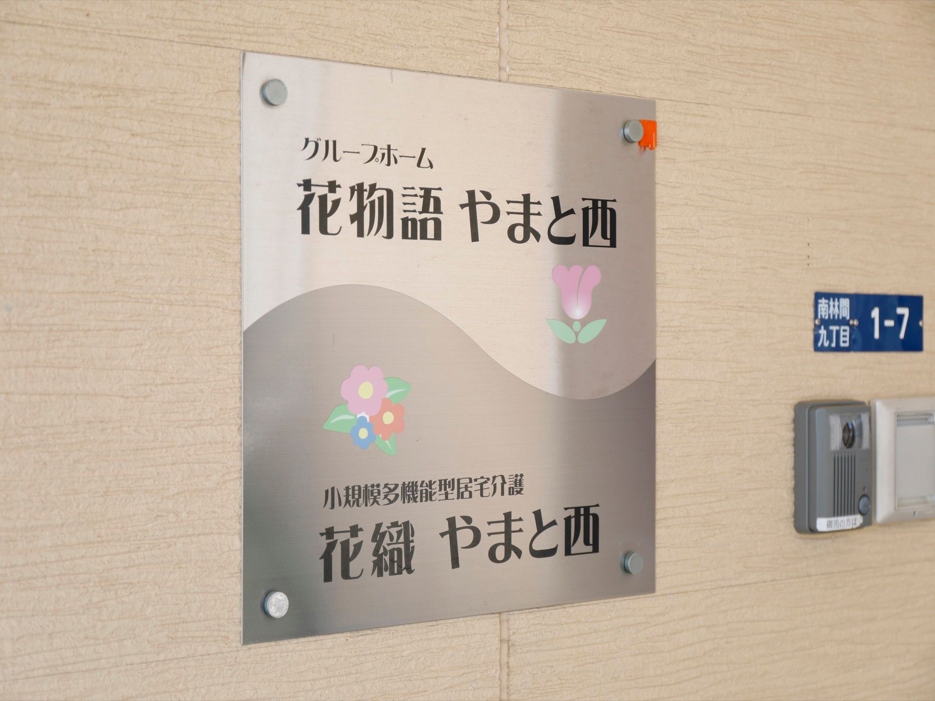 インターフォンの隣には、銀色のプレートがある。ホーム名と施設名が表記されており、花のマークが描かれている。