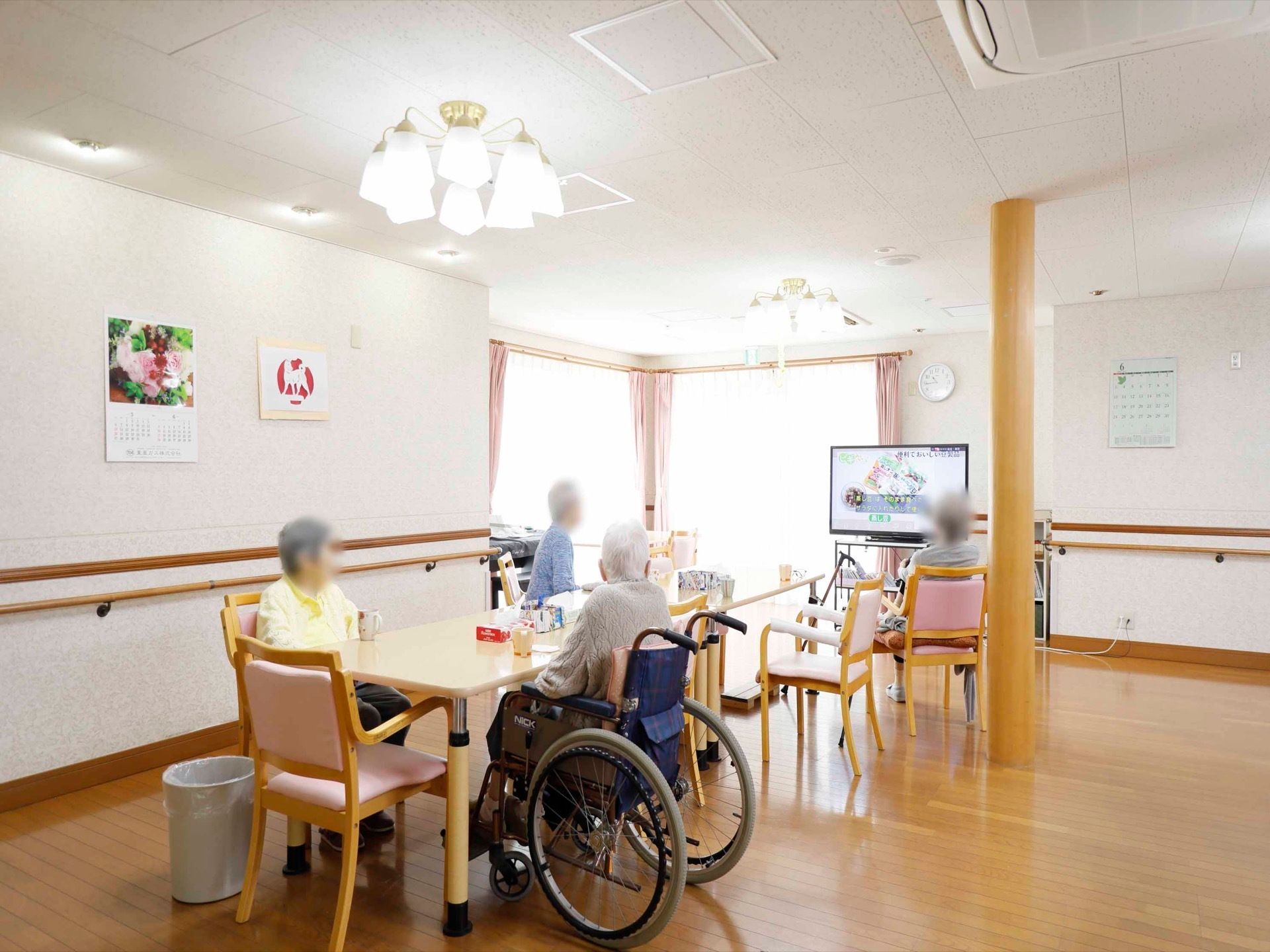 大きな窓があり、外から多くの光を取り入れることができる共有スペースである。入居者様がテレビを視聴している。