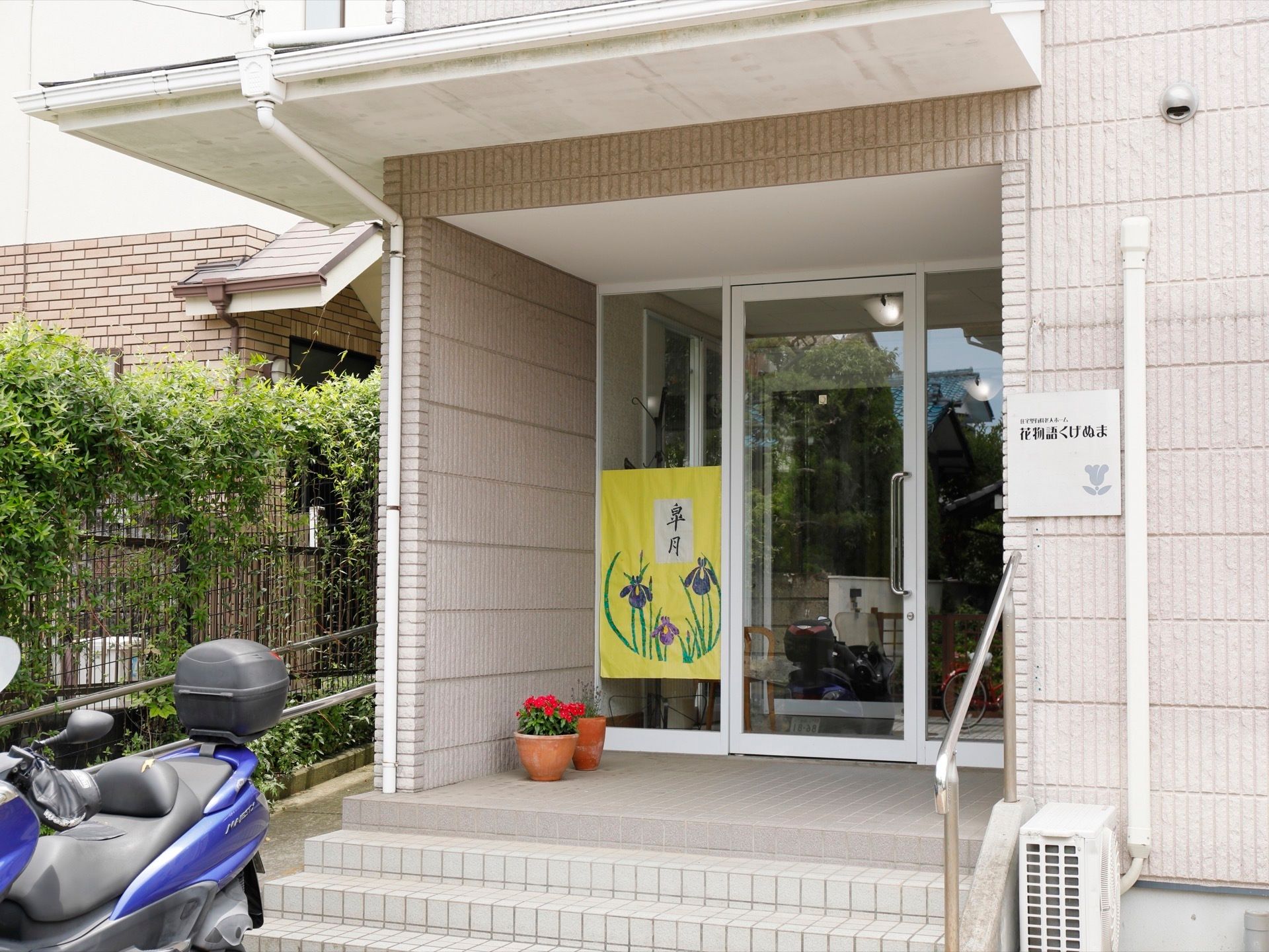正面玄関の階段がある側の様子。すぐ下にはバイクを駐輪できるスペースがある。右には施設ロゴの入った看板プレートがある。