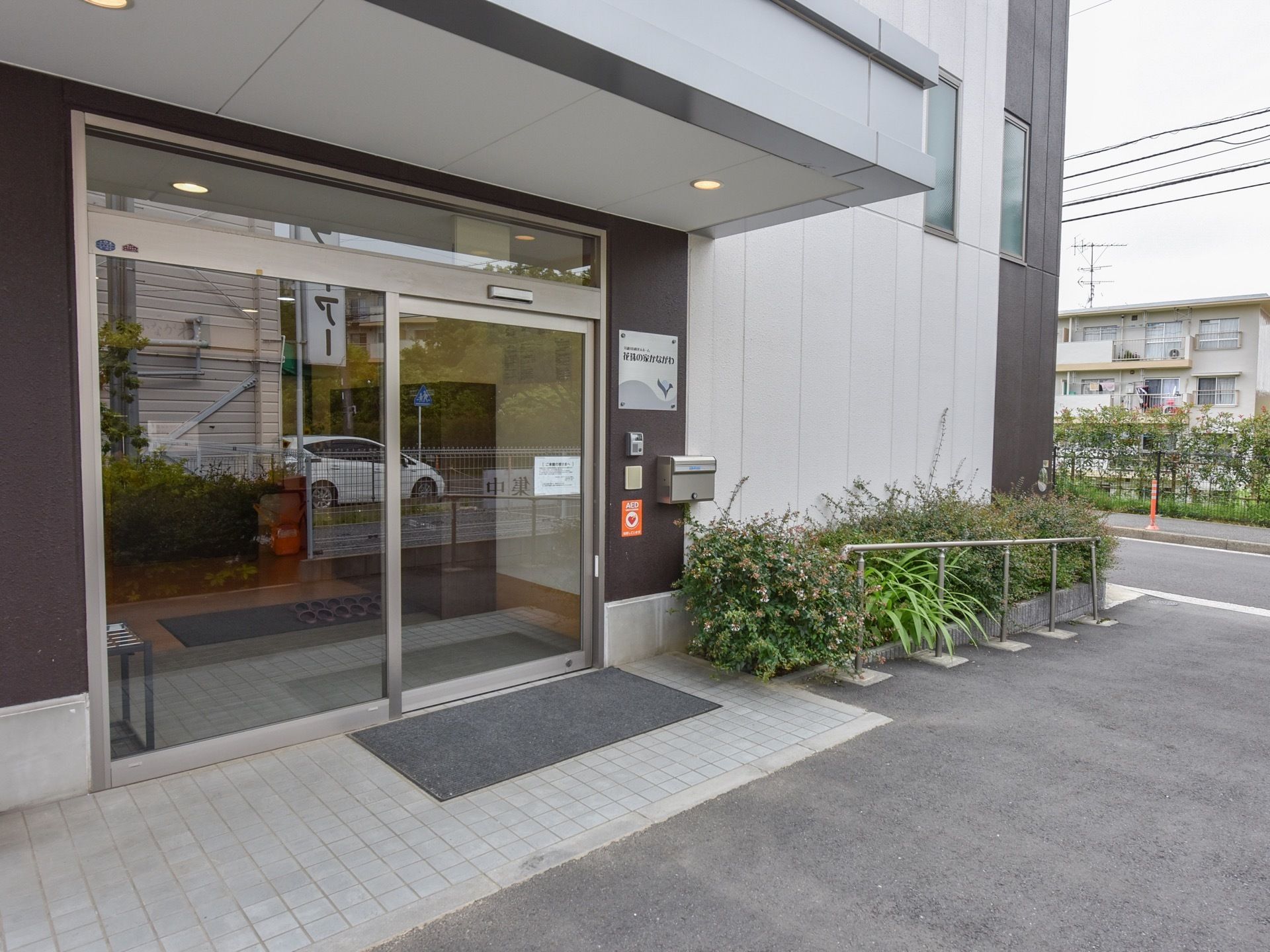 屋根付きの玄関は、ガラス張りの自動ドアを取り入れている。グレーのマットを敷設し、横側の壁に郵便受けを取付けている。