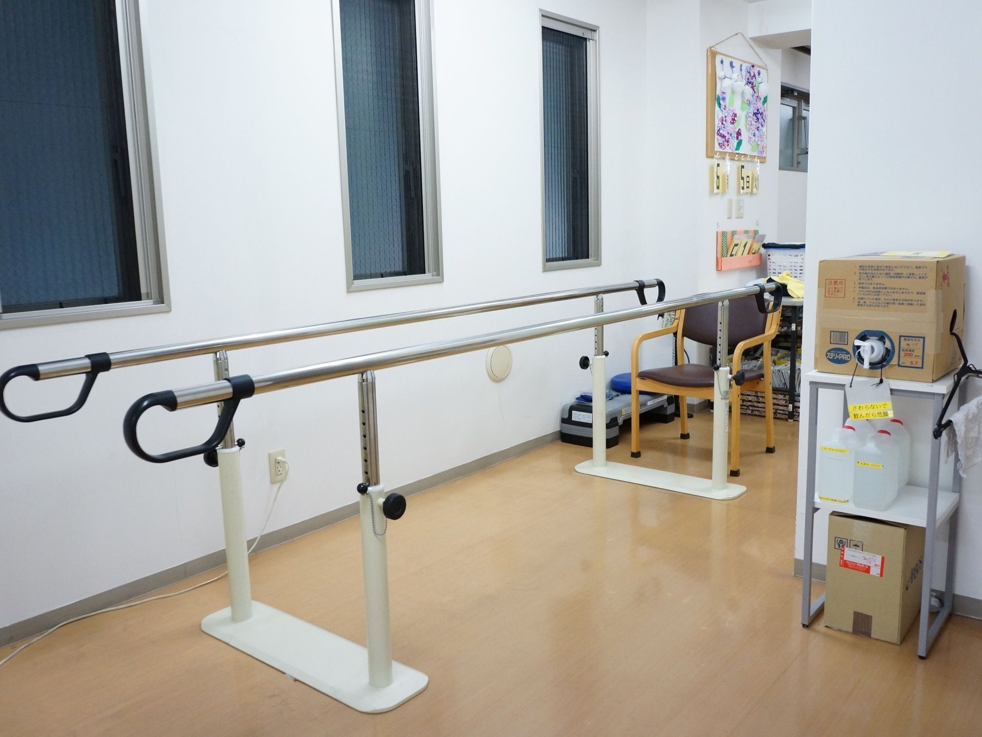 椅子が置かれており、その前に歩行訓練リハビリ用の平行棒が置かれている。平行棒は高さを変えられるものになっている。