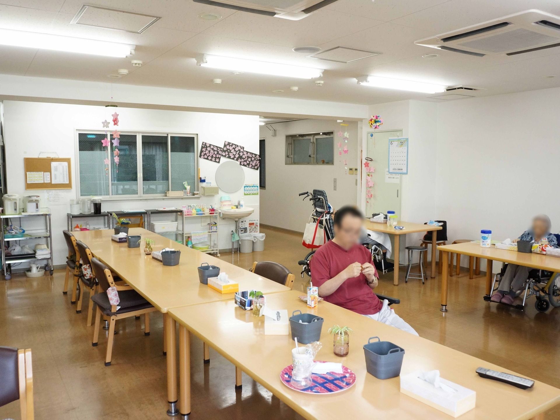 テーブルがいくつか並んでおり、入居者様が席に着いている。テーブルは車椅子でも利用可能なものになっている。