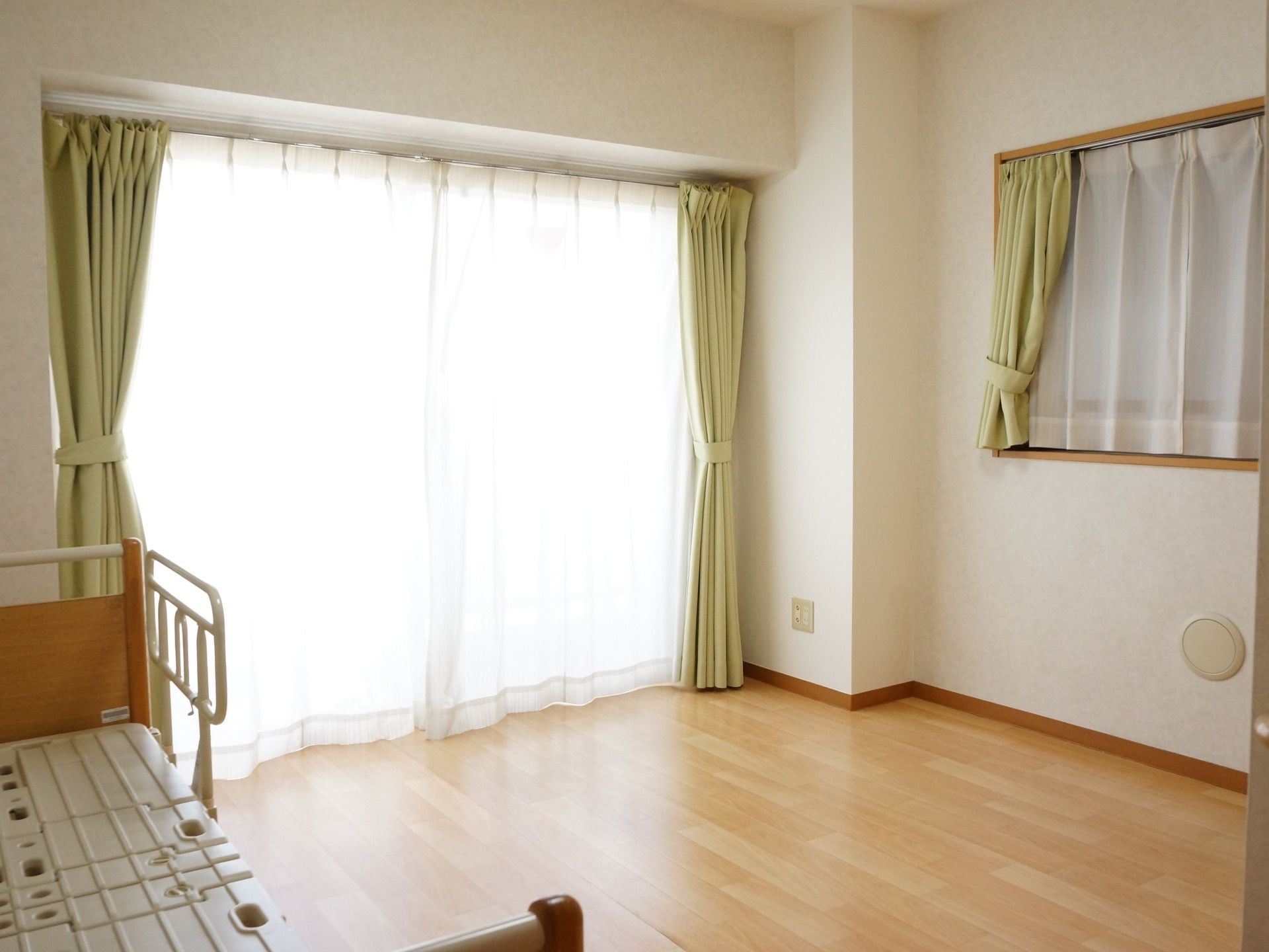 床面はフローリングで、室内の複数の窓には若葉色の明るいカーテンが留められている。ベッドには転落防止用の柵が備わっている。