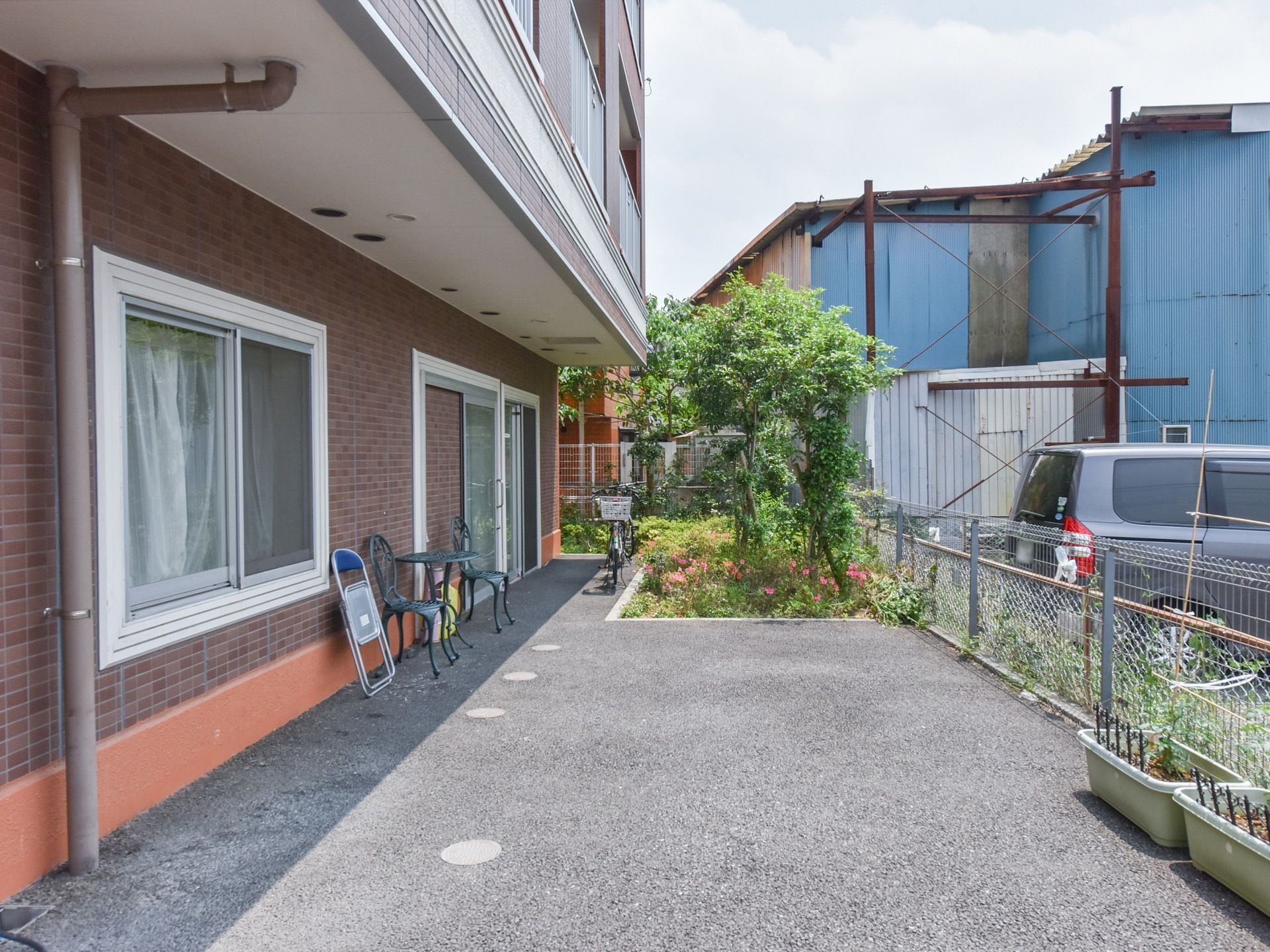 敷地内の奥まった空間には、草木が豊かに生い茂っている。建物の屋根で日陰になっている部分には、１組の椅子とテーブルのセットが置かれている。