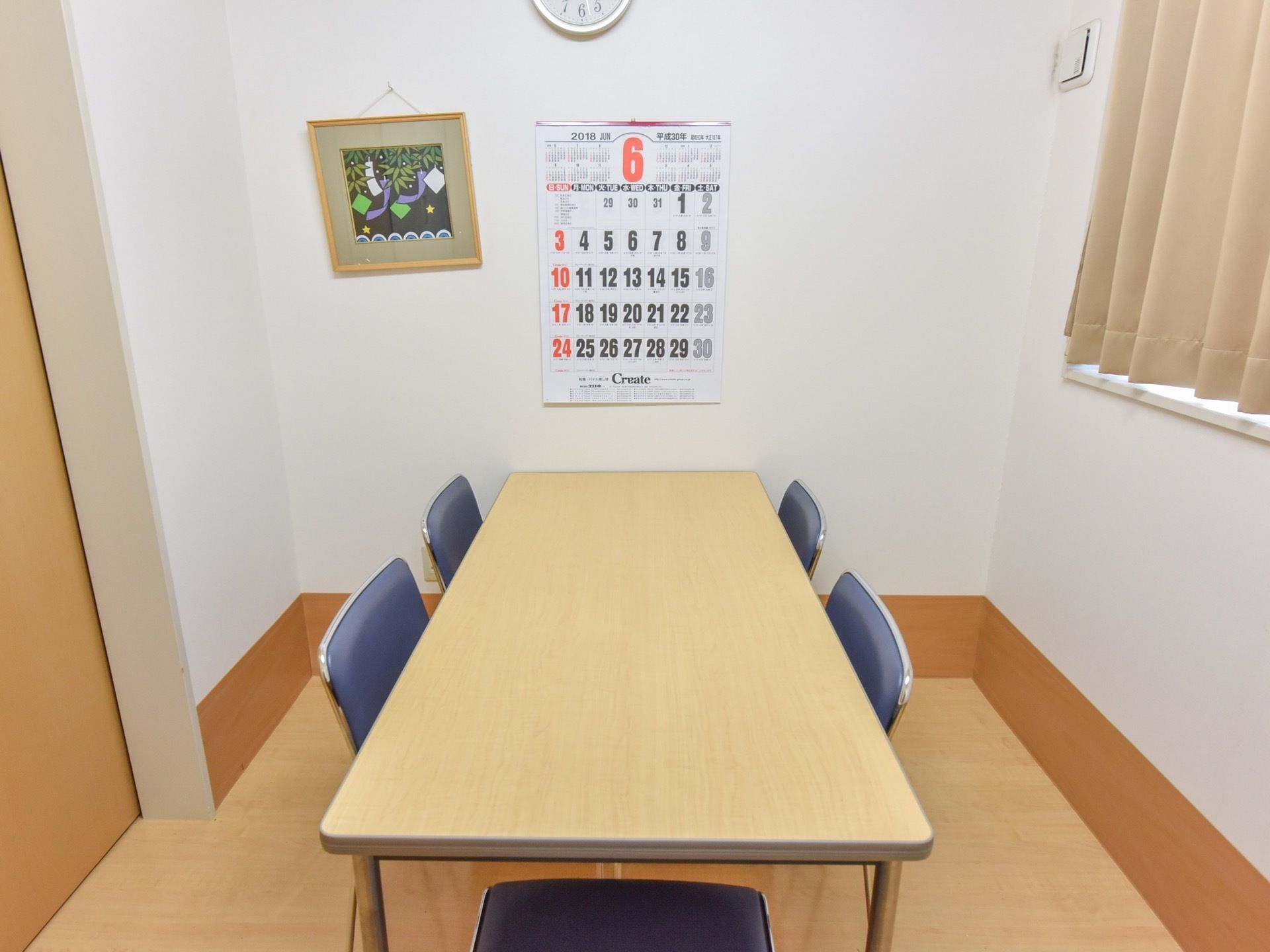シンプルな造りの相談室である。５人掛けテーブルが置かれている。絵画や時計、カレンダーが壁に取り付けられている。