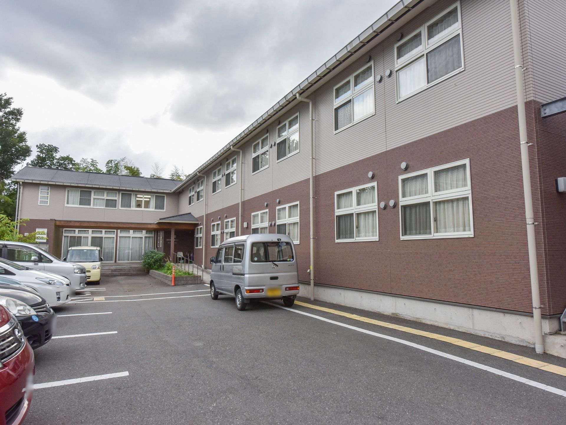 外観がブランウンとベージュ色をした２階建ての施設である。駐車スペースが建物前に設けられている。エントランスには、スロープが設置されている。