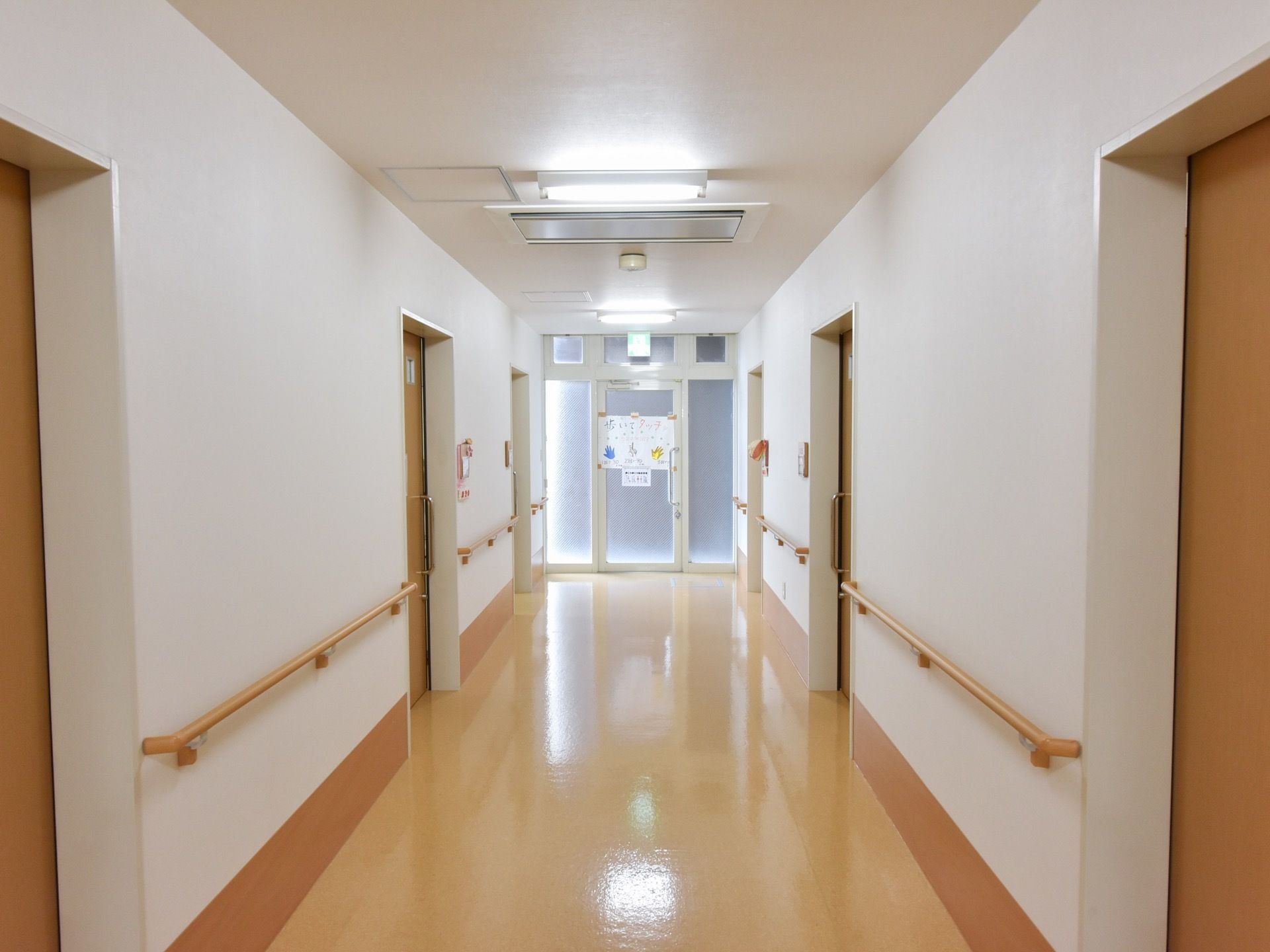 幅の広い廊下である。両サイドに居室の扉が並んでおり、手すりが壁に沿って設置されている。突き当りには、非常口がある。