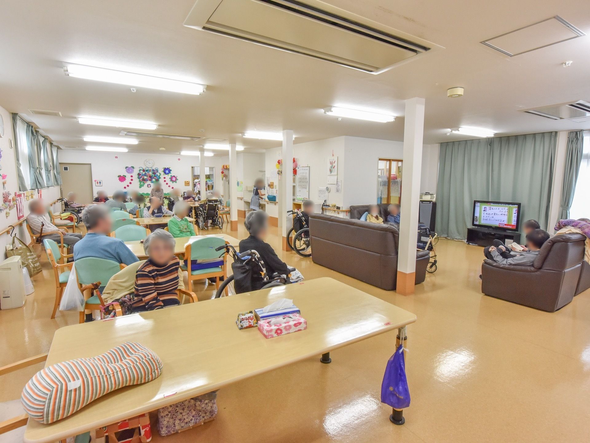 広々とした食堂兼リビングには、複数のテーブルや椅子、ソファが置かれている。窓際に大型テレビが設置されている。