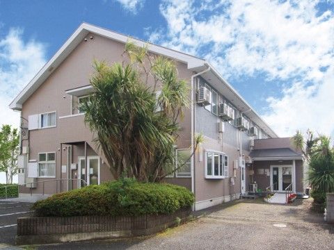 背の高い植木のあるアプローチと三角屋根が特徴な２階建て施設の外観