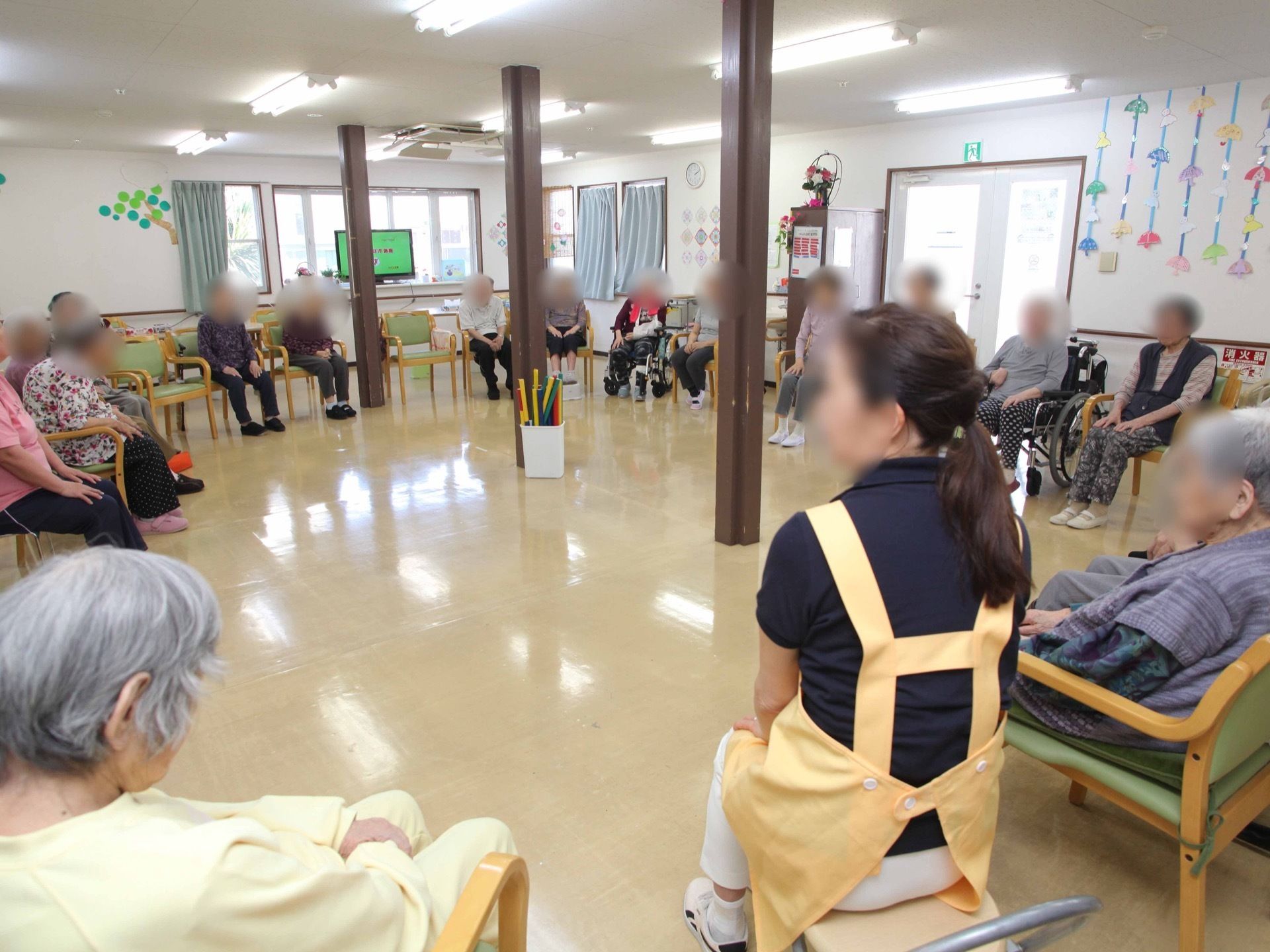 大人数が集まっても、ゆとりのある空間を確保している。黄色のエプロンを着用したスタッフとともに、入居者様がイベントを楽しんでいる。
