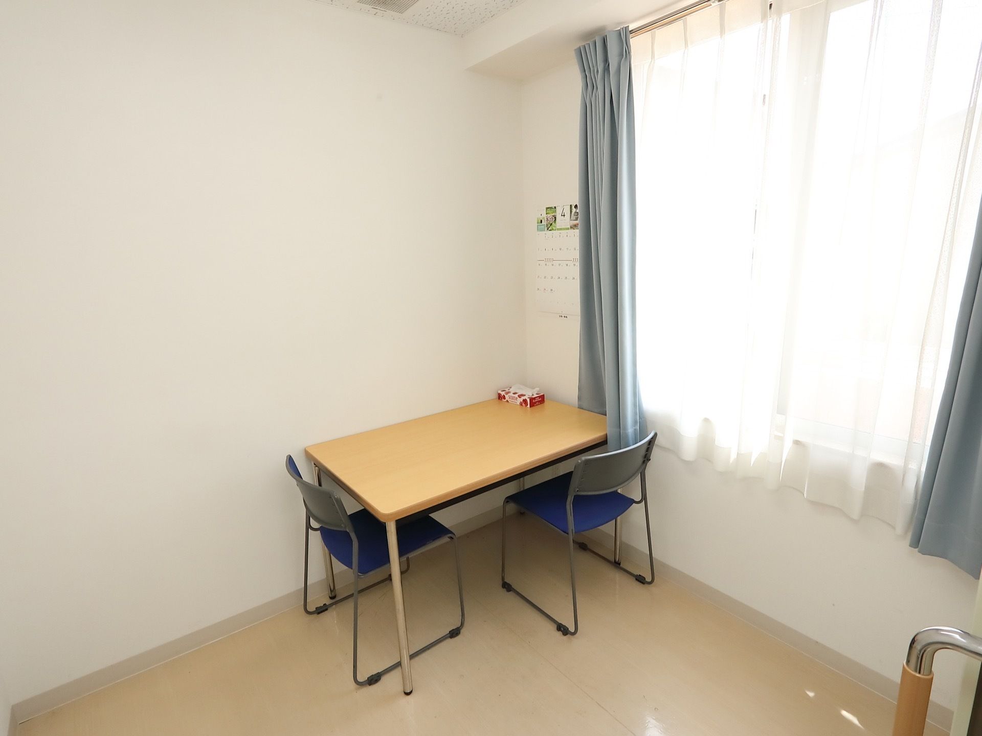 大きな窓からの日差しで明るい談話室がある。部屋の隅にテーブルがあり、２つの椅子が壁に向かって置かれている。
