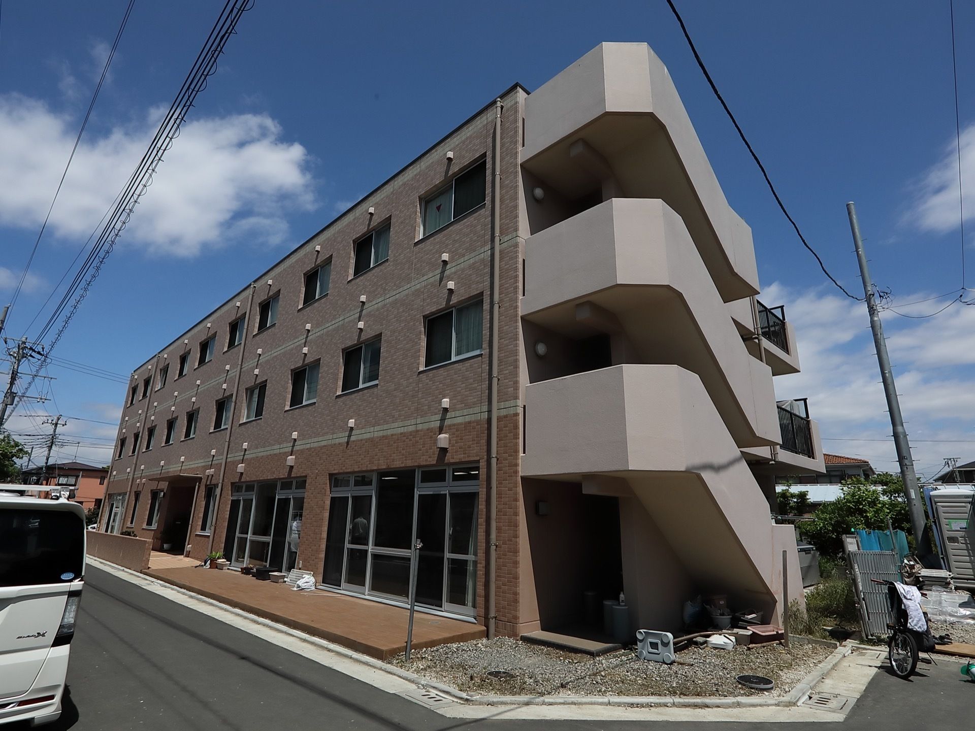 茶色系統を基調とした３階建ての施設である。幅の広い外階段がある。玄関の前の道路との境界には低い壁が造られている。