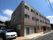 茶系統の色を基調とした３階建ての施設である。玄関前には低い壁が造られている。建物横に車が２台停まっている。
