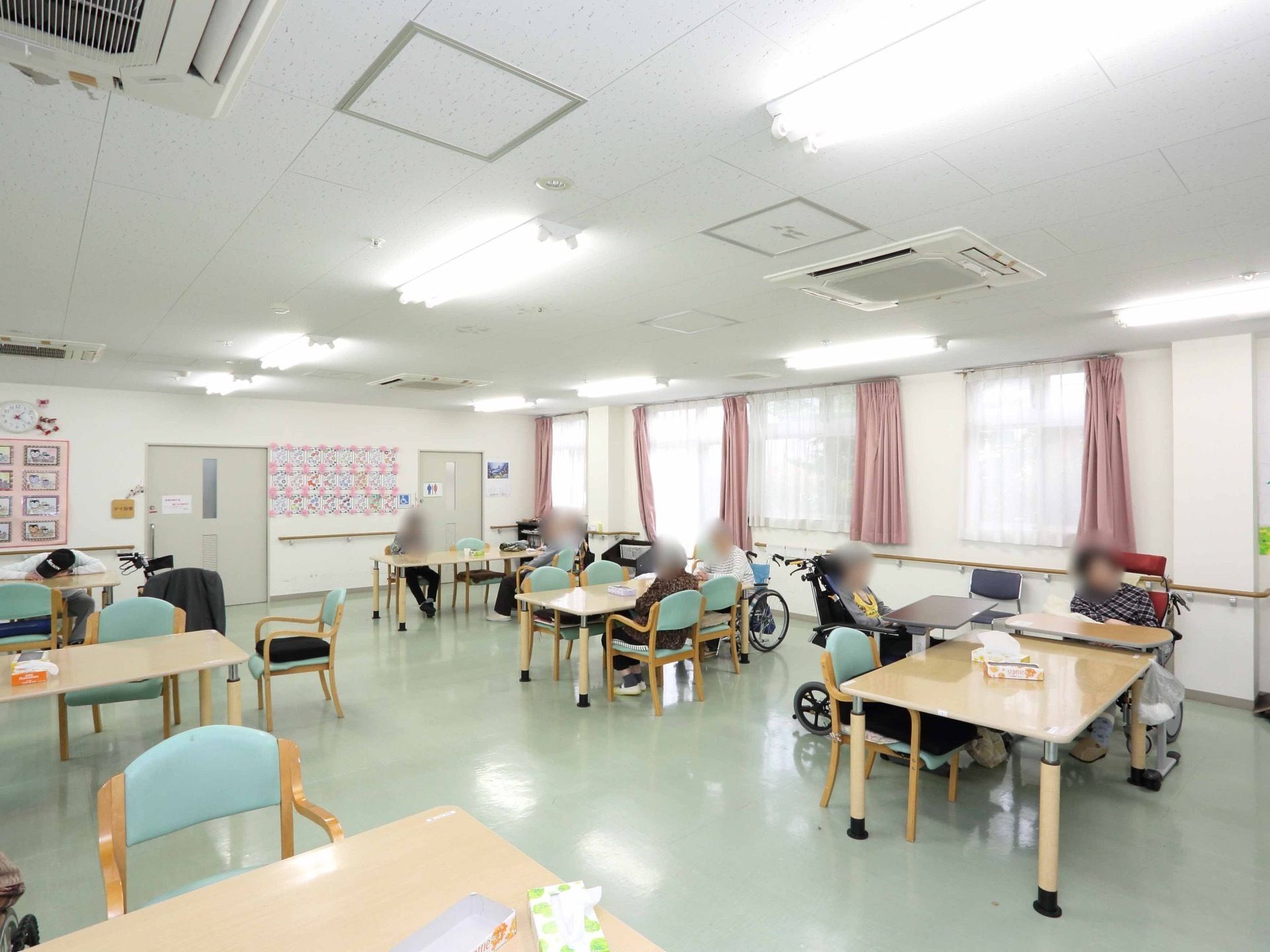 完備された窓には白いレースのカーテンが引かれ、ピンクのカーテンが両端に寄せられている。テーブルセットの椅子のシートは、パステルグリンである。
