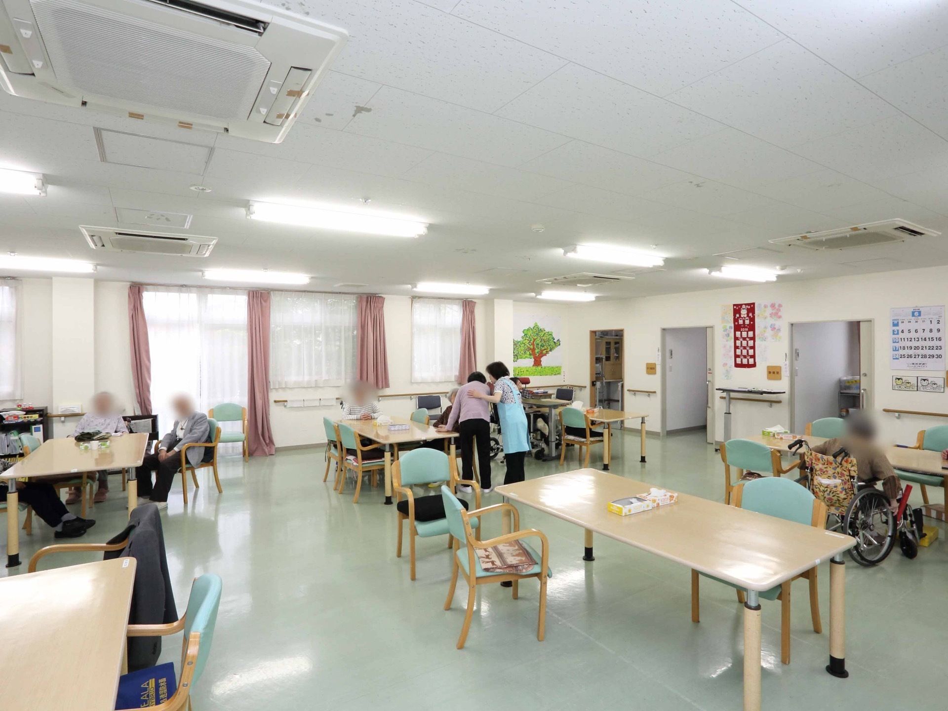 とても広い共有スペースである。ダイニングテーブルが間隔をとって配置されている。壁には手すりがあり、天井には空調が付いている。