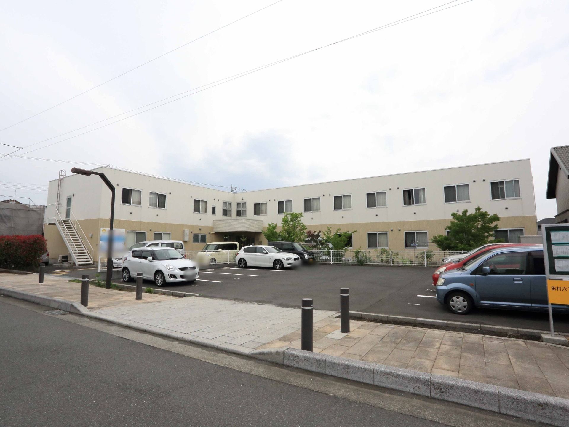 窓の多い2階建ての建物で、非常階段も設置されている。駐車場も完備されているので、来訪者様も気軽に来ることができる。