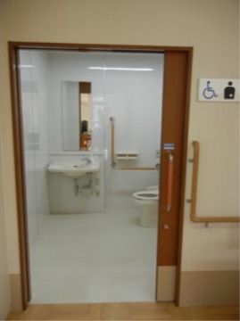 洋式の便器と洗面台が備わるトイレのドアはスライド式である。トイレのドアの横の廊下の壁には手すりが設けられている。