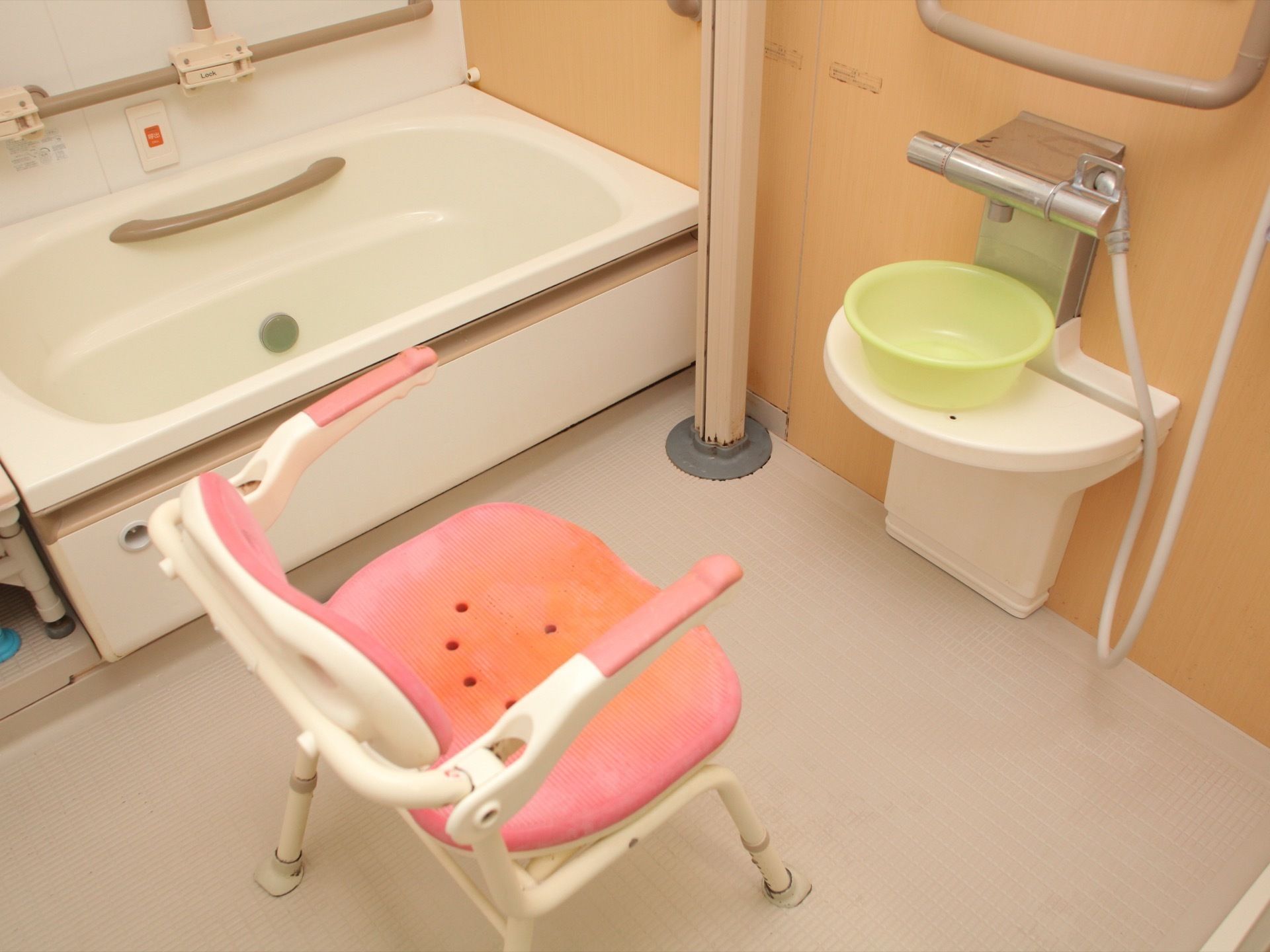 肘掛けの付いたシャワーチェアが置いてあり、前の台には洗面器が備えてある。浴槽側の壁には、手すりや呼び出しボタンが設置されている。