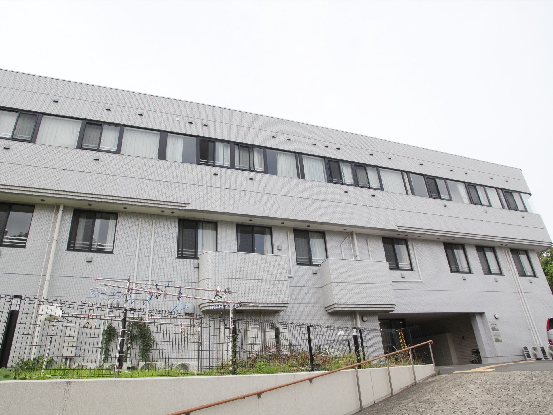 道路から建物へ入っていくところは坂になっており、手すりが付いている。外には物干しざおがあり、ハンガーなどが掛けられている。