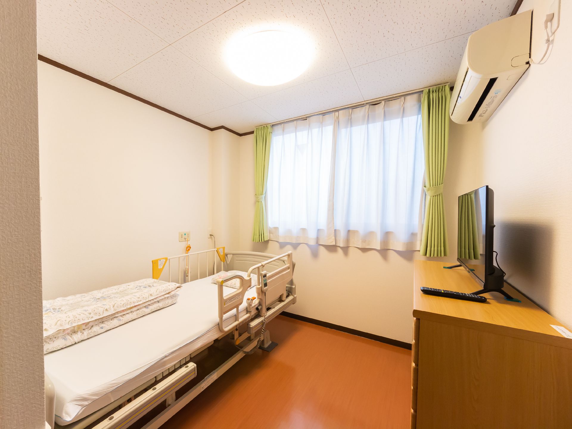 窓から日差しが降り注ぎ、介護ベッド、エアコンが設置されている居室