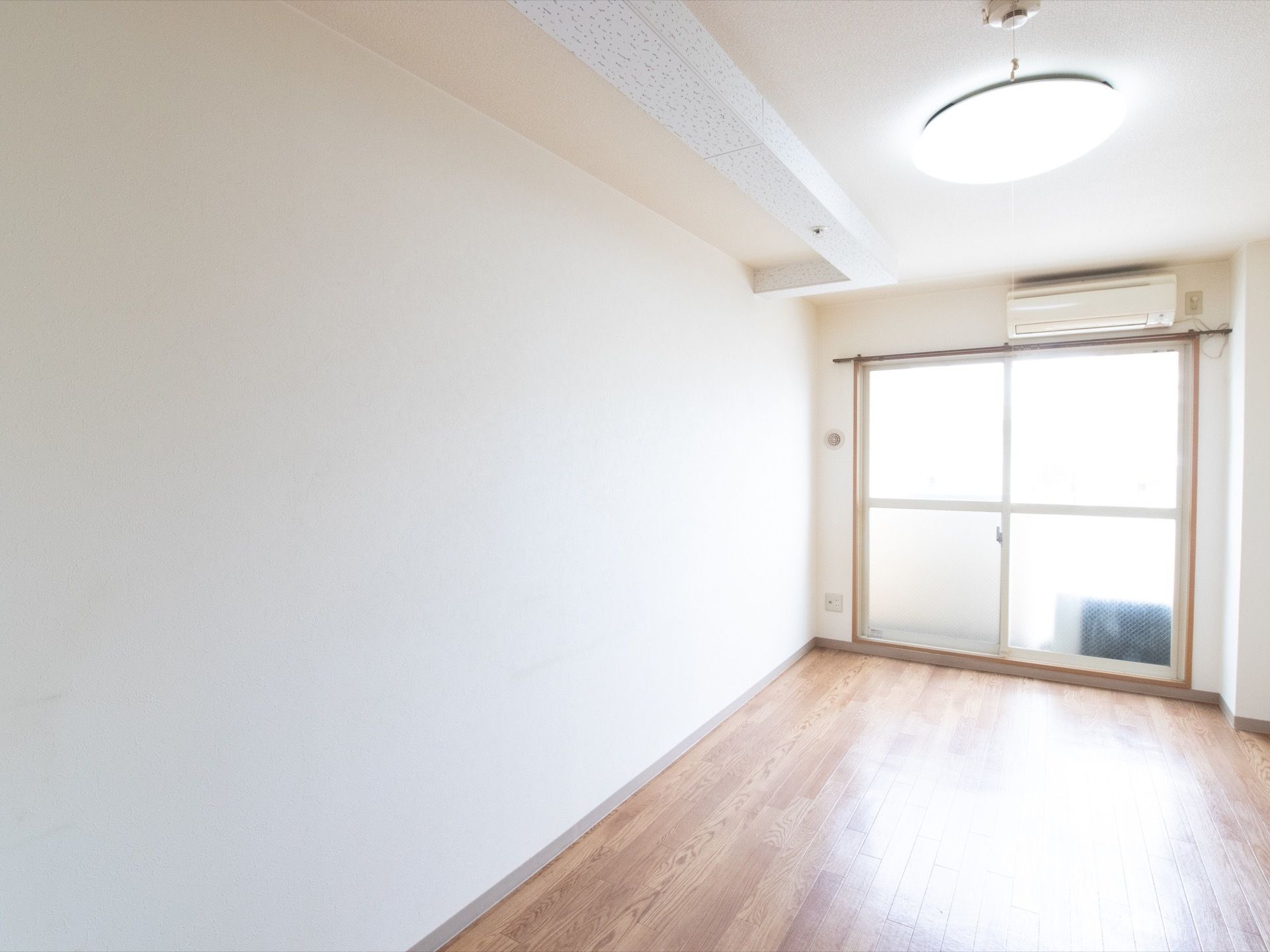 居室の奥には窓があり、外へ出ることができる。窓の上にはエアコンがある。壁の低いところにコンセントがついている。