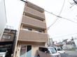 茶系の外壁のスマートな４階建ての建物である。建物の前には駐車場が設置され、軽自動車が１台停まっている。