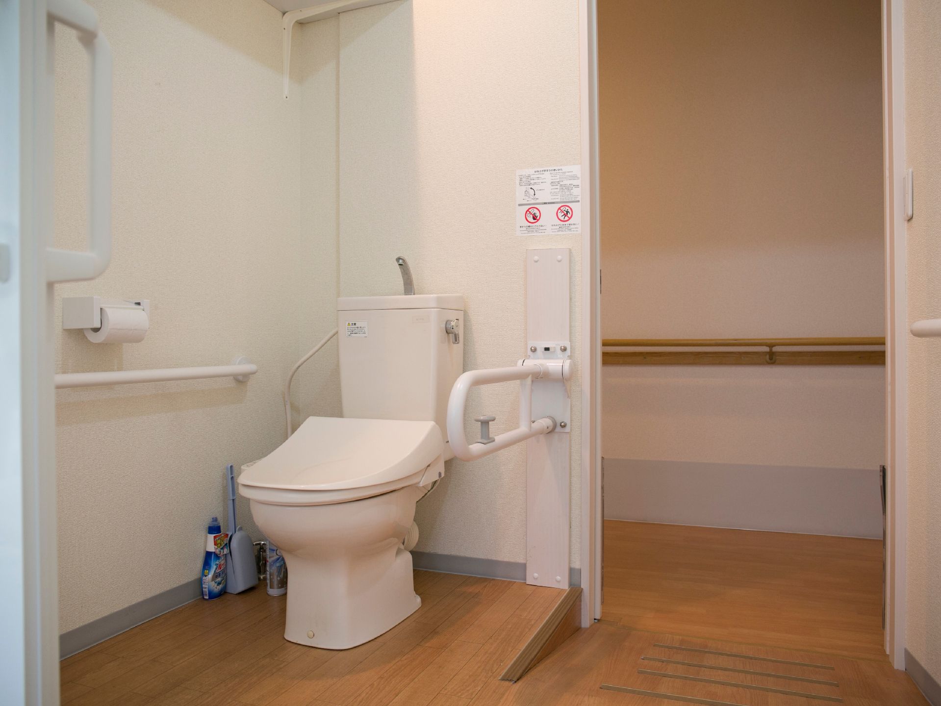 廊下側から少し高くなっているフロアにトイレが設置されている。左右には手すりがあり、上部には棚が設けられている。