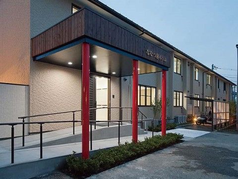 手すり付きスロープがエントランスまで続いている、赤い柱が印象的な外観の建物