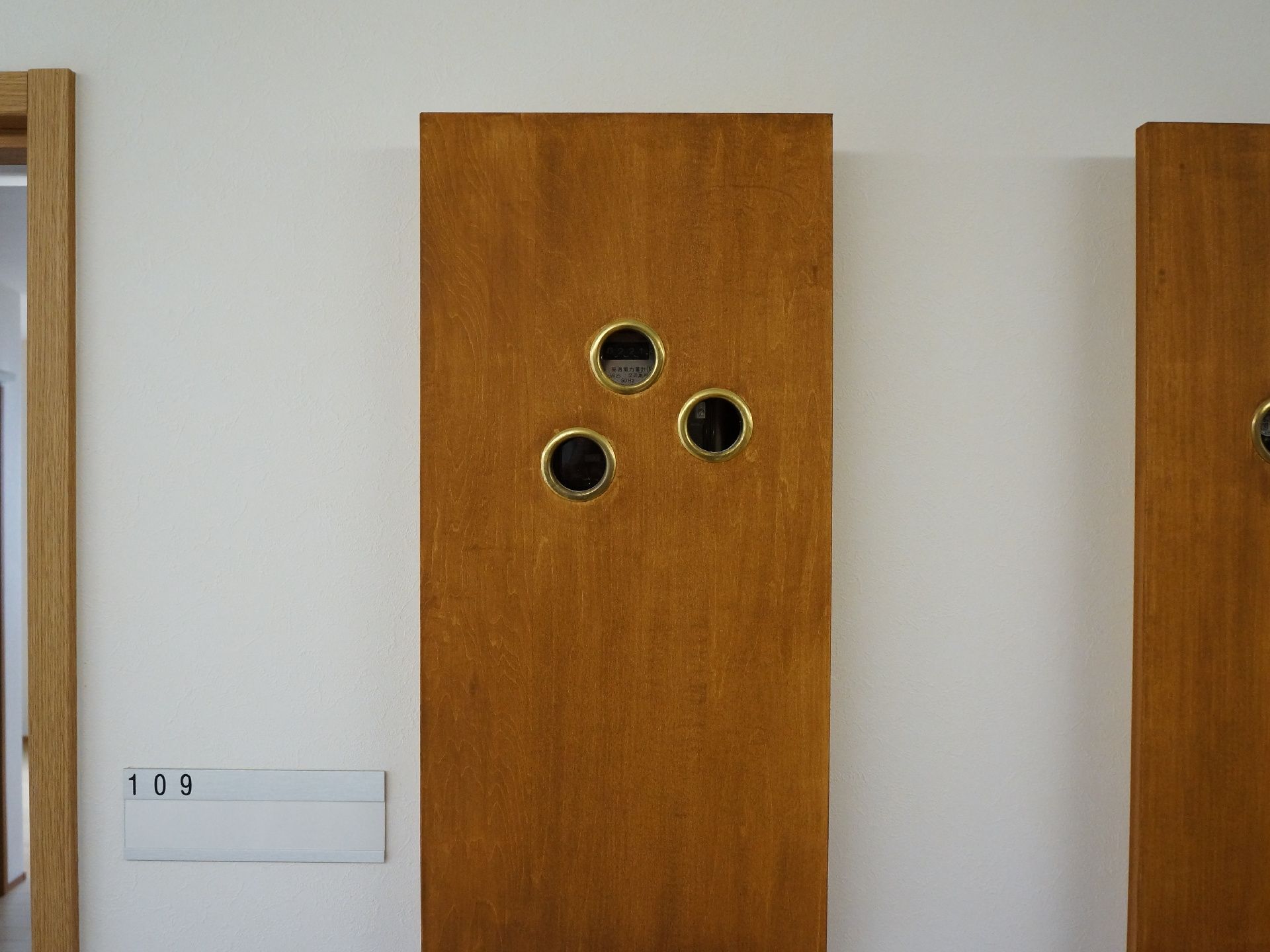 廊下の壁の色は白で、部屋番号が入った名前用のプレートが設置されている。入り口ドアの縁などには木材が使われている。